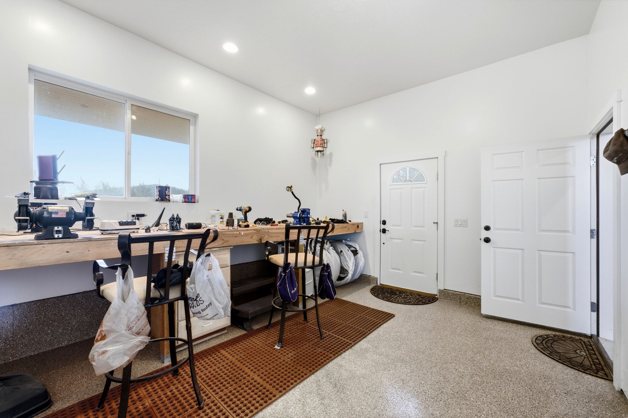 Light-filled utility space featuring an epoxy-coated floor, a large sliding window, recessed lighting, a built-in workbench, and multiple panel doors