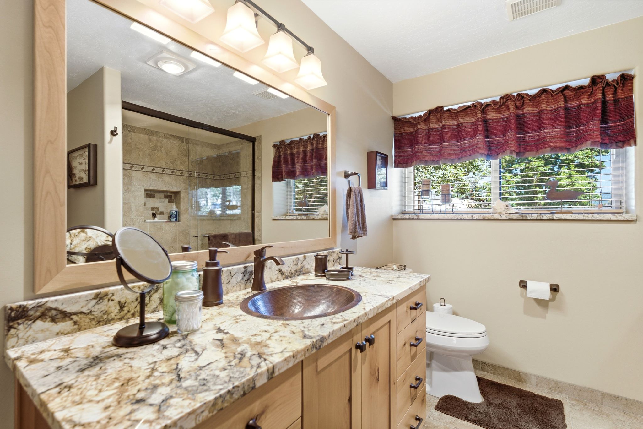 Bathroom vanity featuring a copper basin sink, light wood-finish cabinetry with dark hardware, a spacious granite countertop, and an oversized mirror