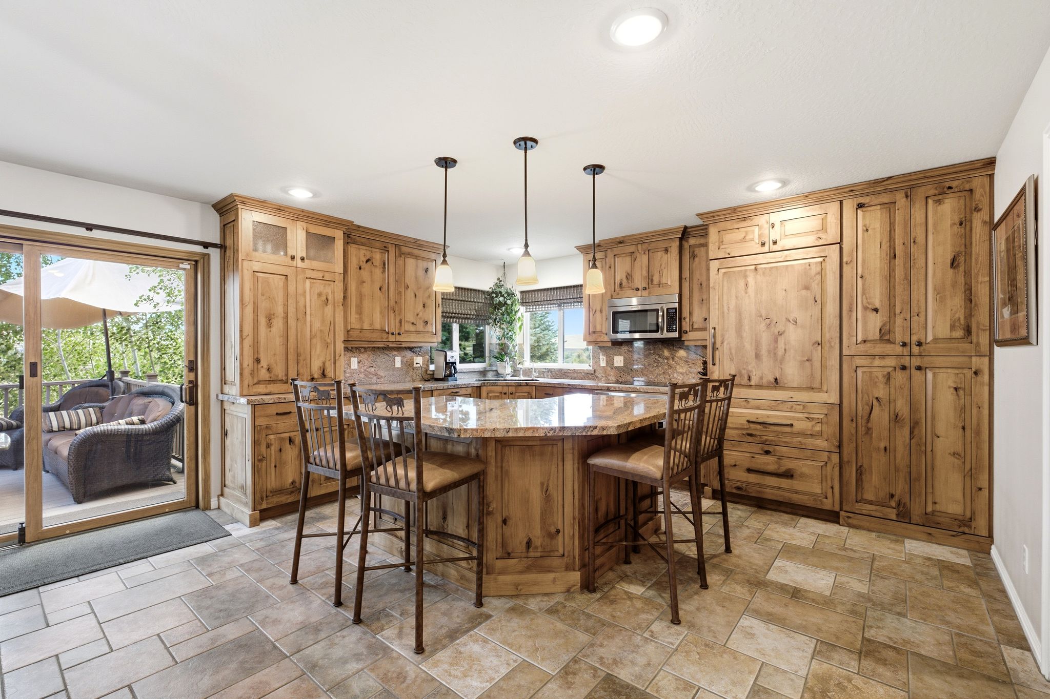 Kitchen featuring an expansive island with a granite countertop, integrated stainless steel microwave, stone tile backsplash, wood cabinetry, and tile flooring