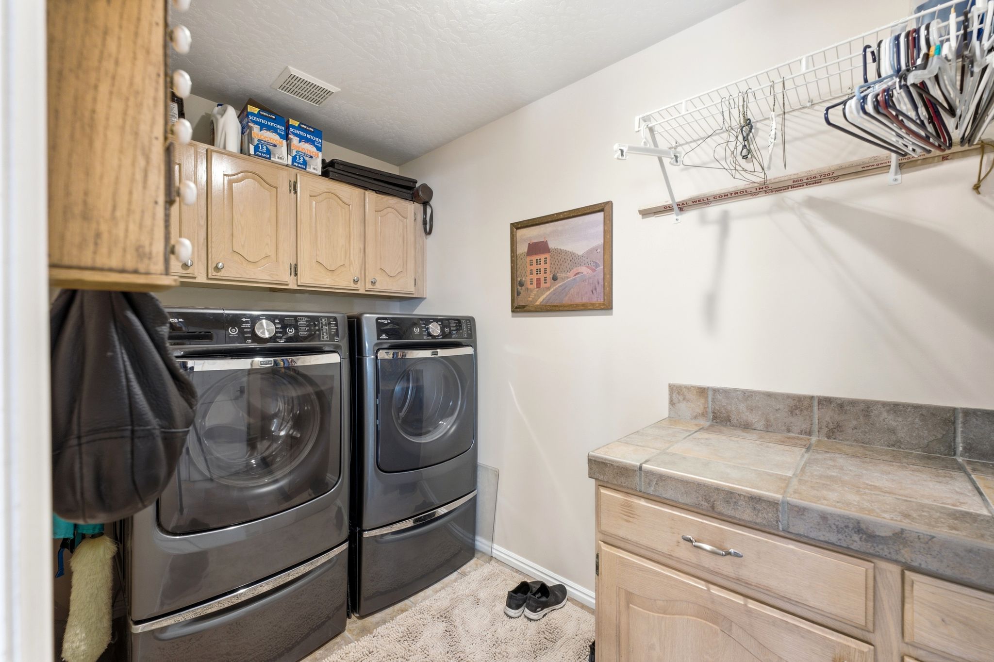 Dedicated laundry area featuring upper cabinetry, a tiled countertop, and a built-in hanging rack