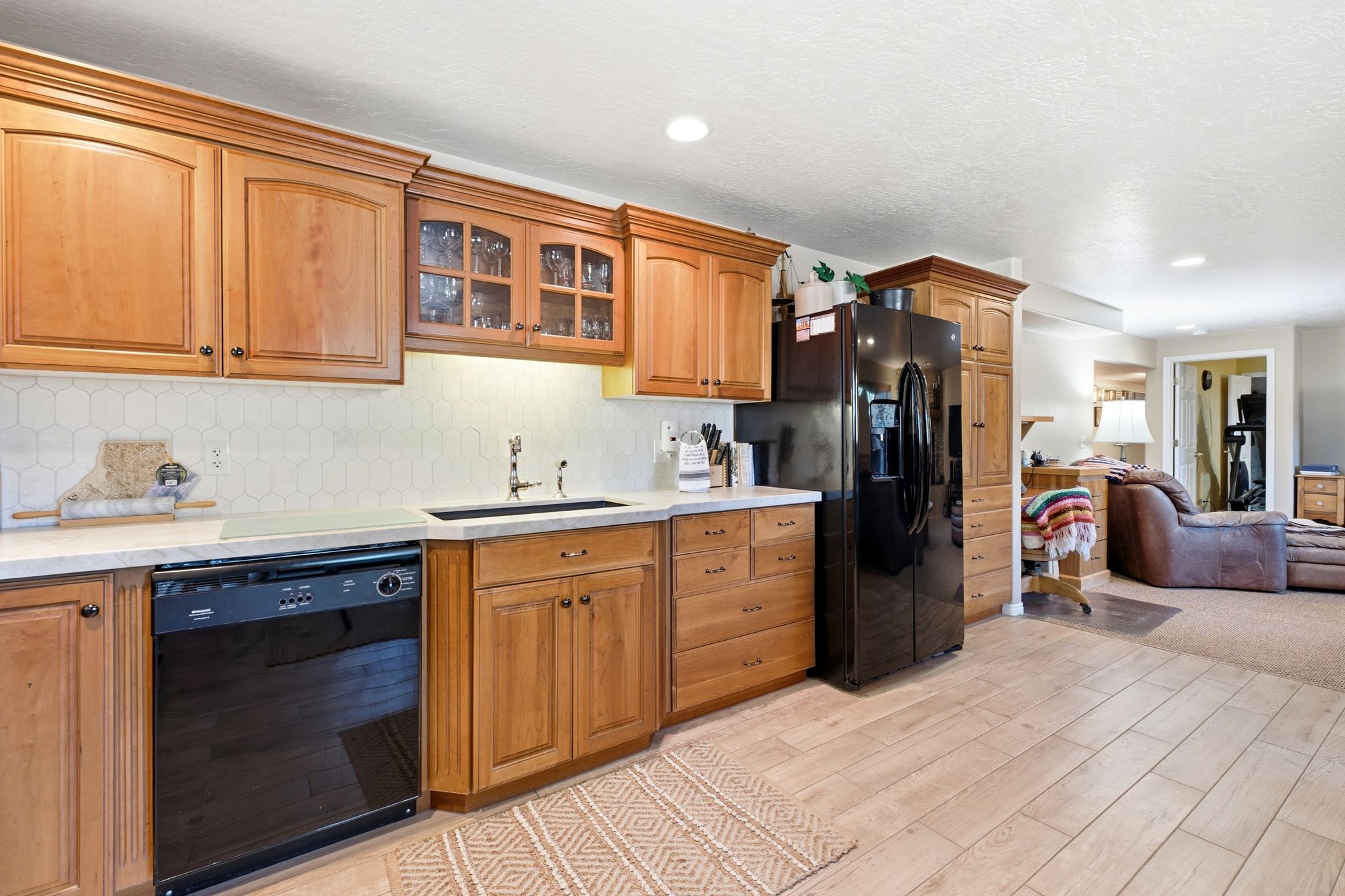 Kitchen featuring light wood cabinetry, white hexagonal tile backsplash, light countertops, and black appliances
