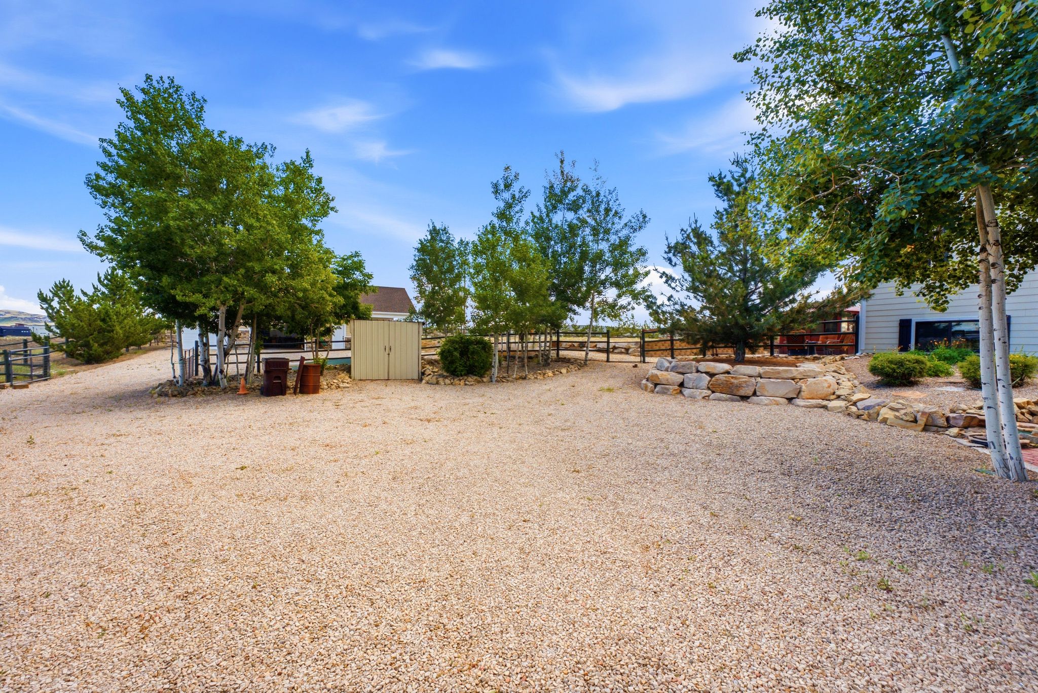 Gravel driveway featuring mature trees, a storage shed, and a stone retaining wall