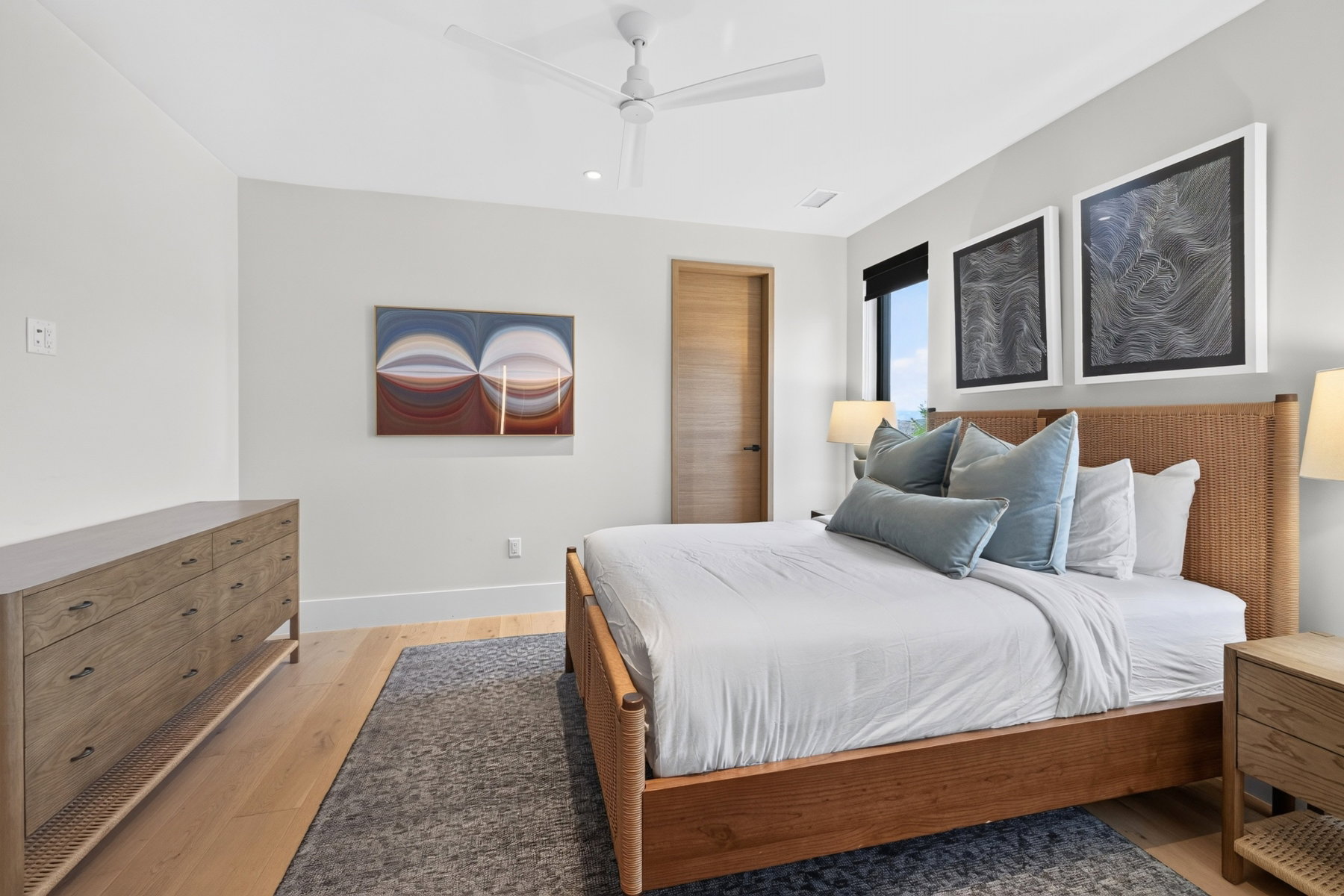 Spacious bedroom featuring light wood-finish flooring, a contemporary ceiling fan, and a light-colored solid wood door