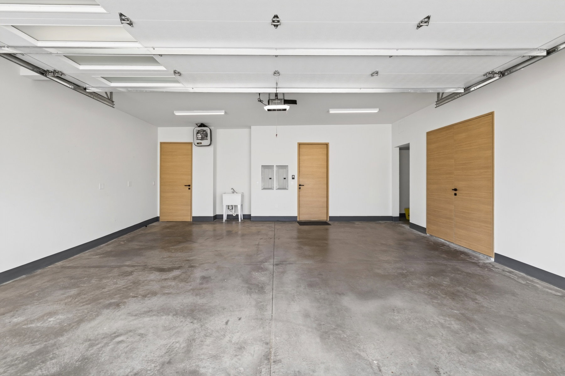 Spacious garage featuring a concrete floor, bright overhead lighting, three wood-finish doors, and a utility sink