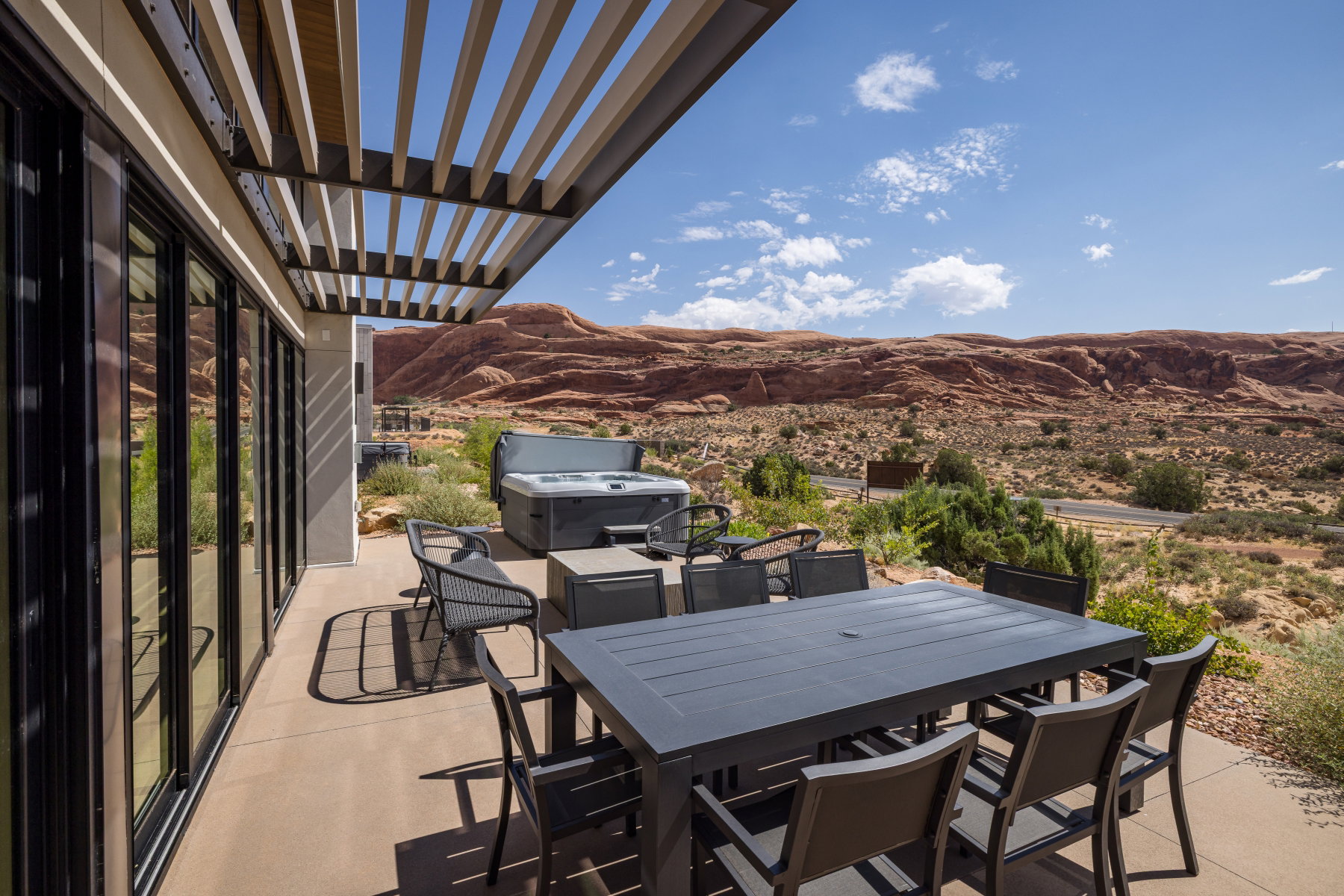 Expansive outdoor patio featuring a slatted pergola, desert landscaping, and distant mountain scenery