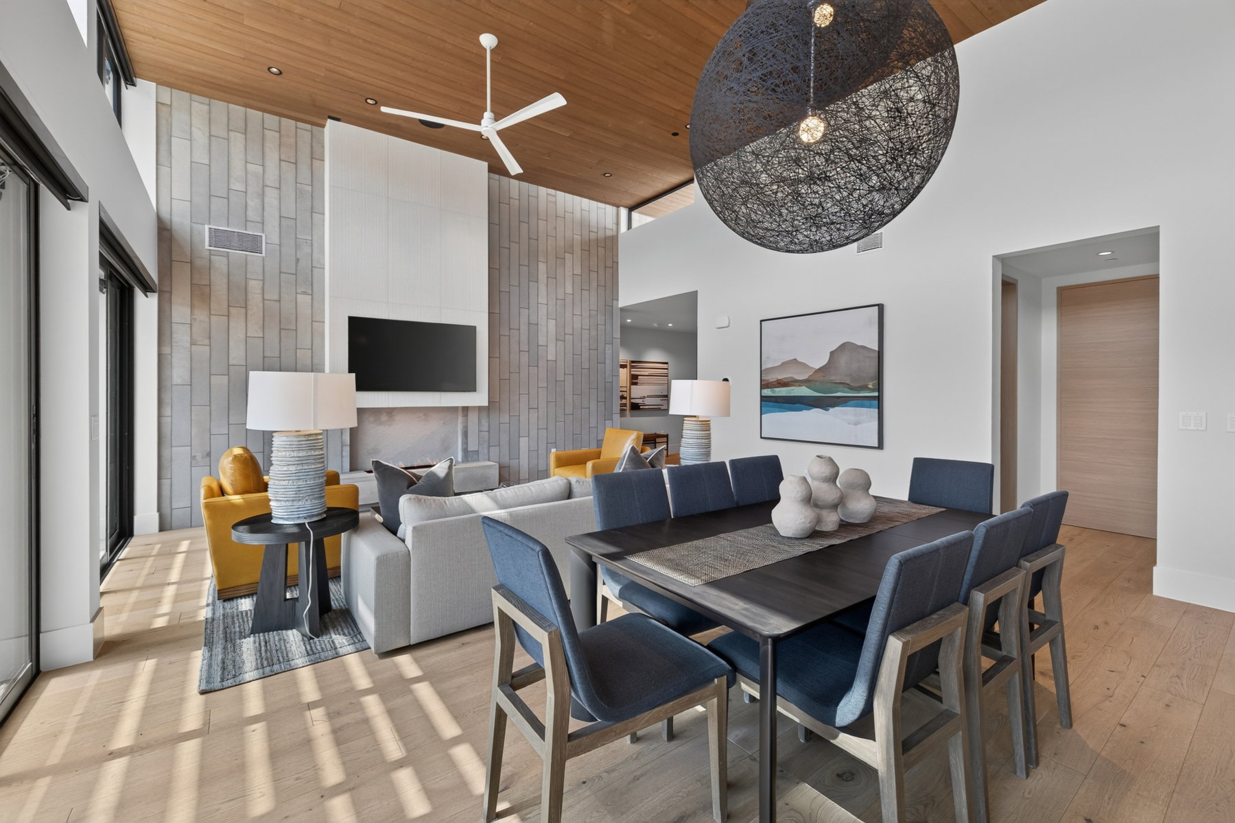 Open-concept living and dining area featuring a wood-finish ceiling, stone accent wall, and light wood-finish flooring