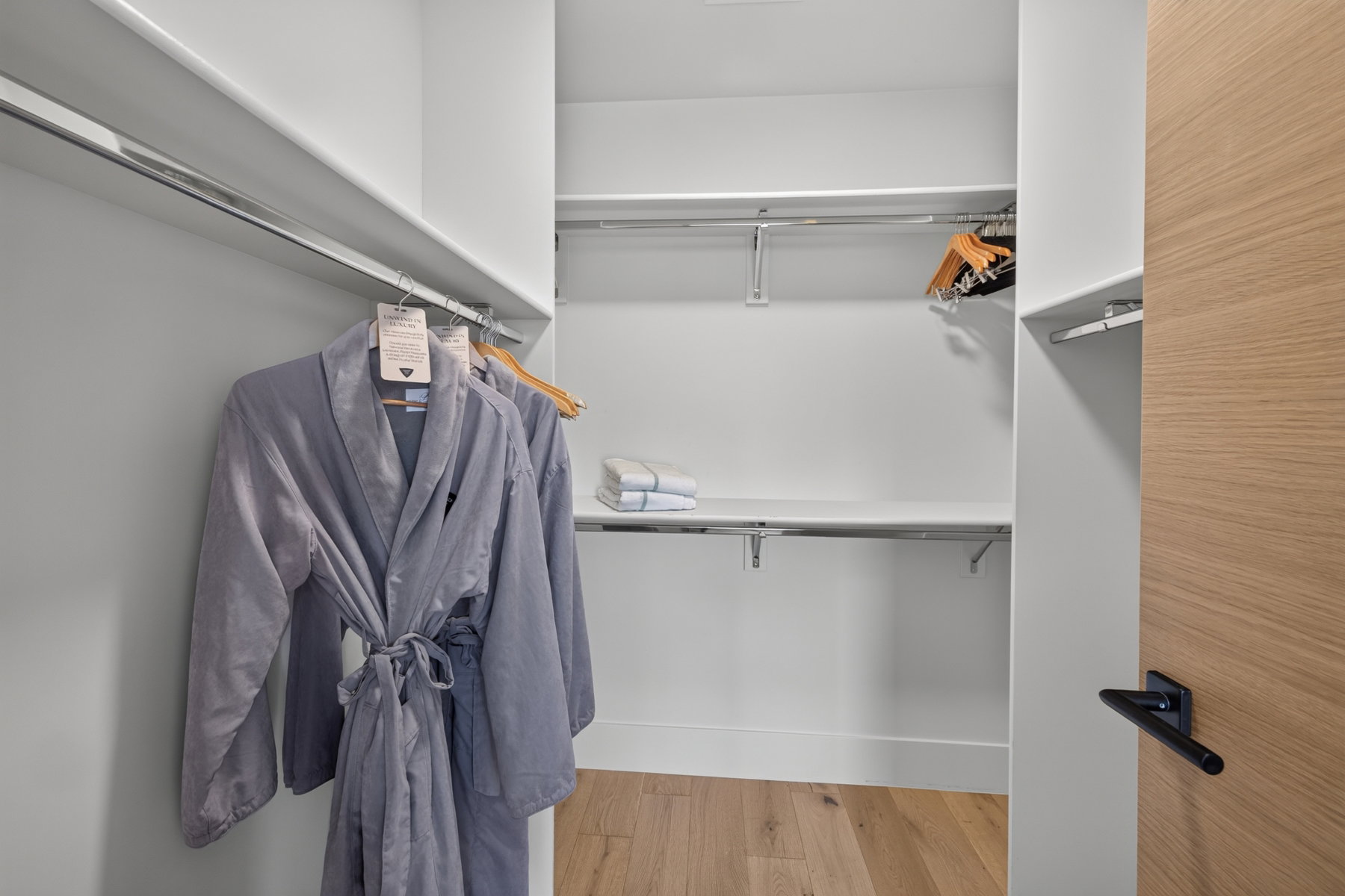 White-painted walk-in closet featuring wood-finish flooring, multiple shelving units, and chrome hanging rods