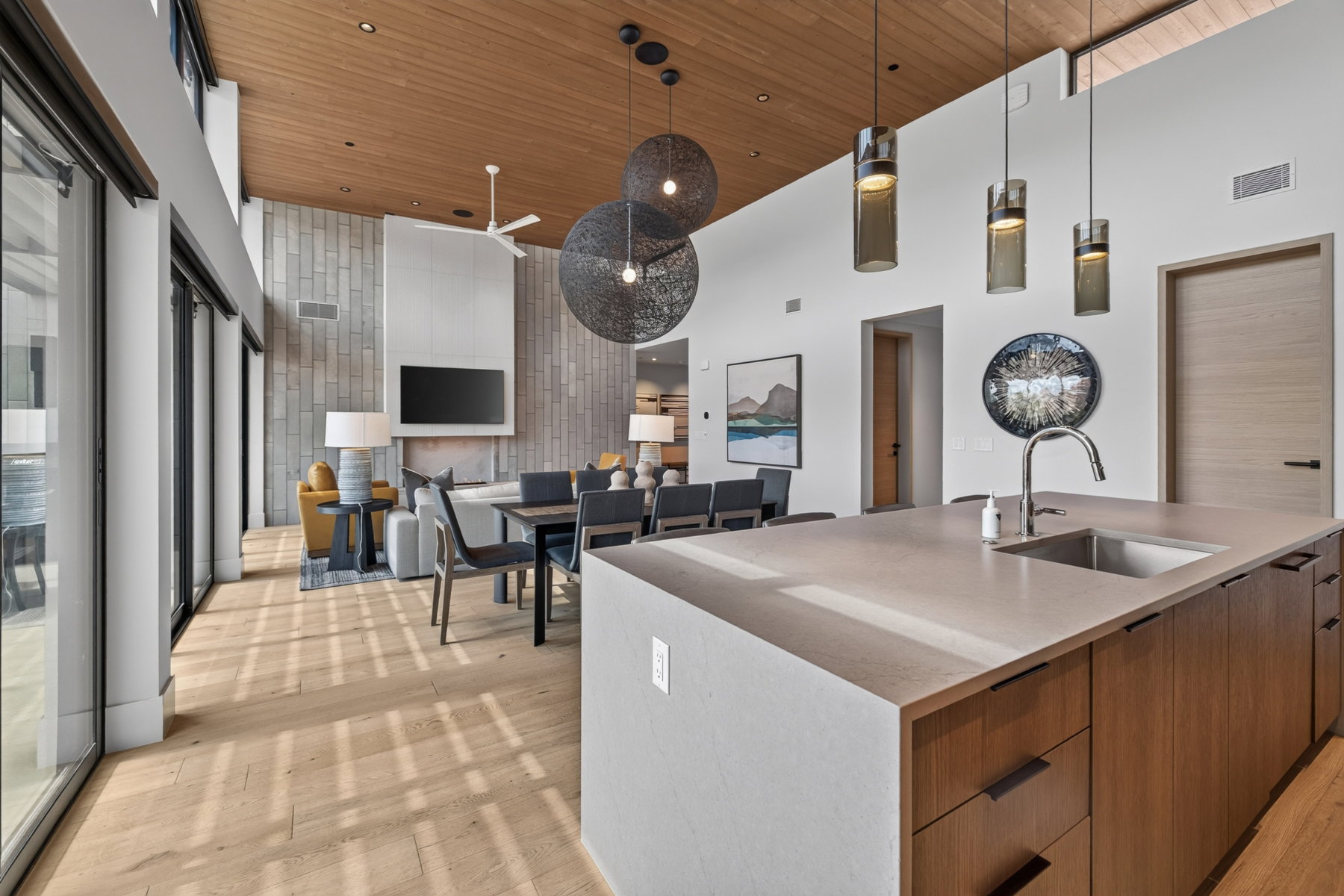 Spacious open-concept interior featuring light wood-finish flooring, a wood-paneled ceiling, and a kitchen island with an integrated stainless steel sink