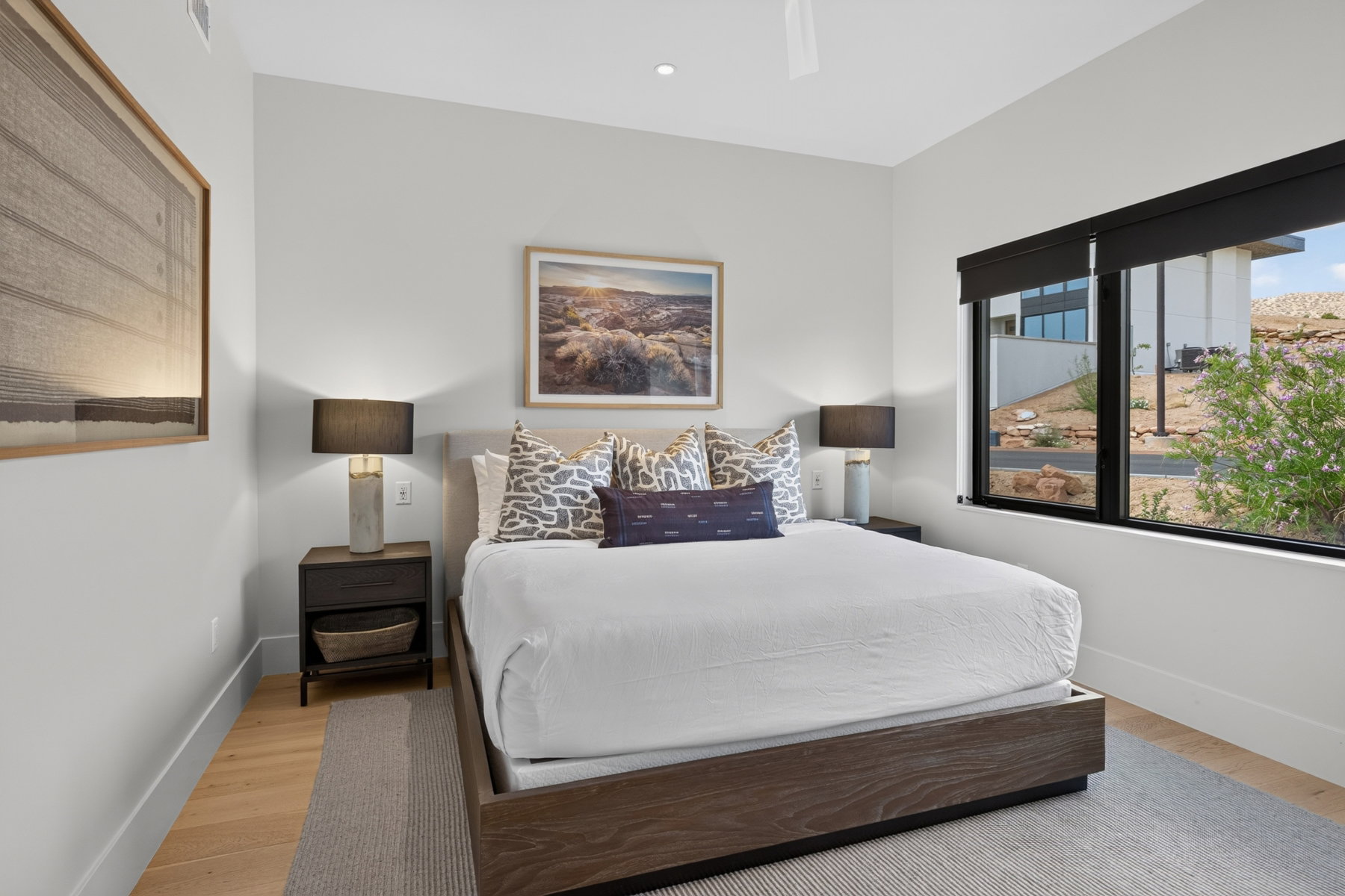 Bedroom featuring wood-finish flooring, a contemporary ceiling fixture, a large window with roller shades, and light-colored walls