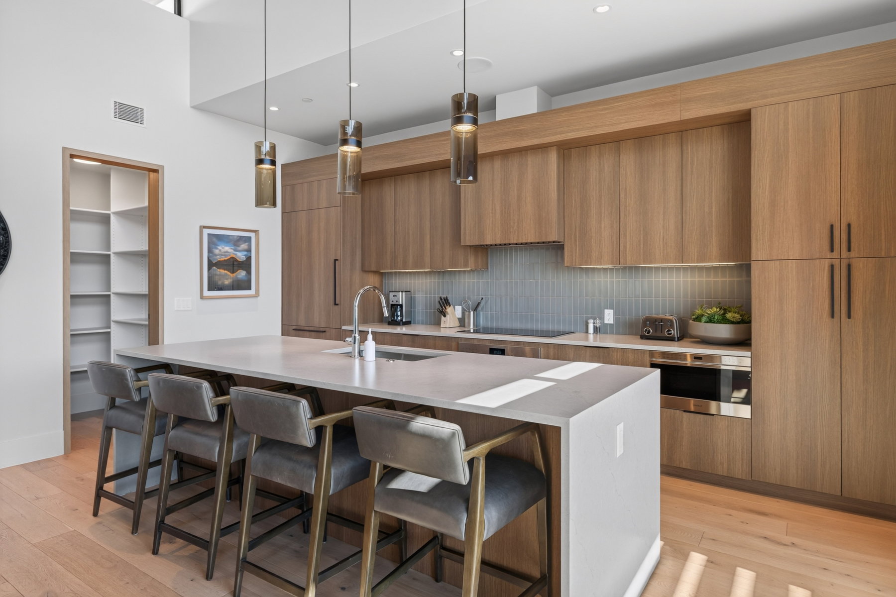 Modern kitchen featuring wood-finish cabinetry, a large center island with integrated sink, stainless steel appliances, a tiled backsplash, and recessed lighting