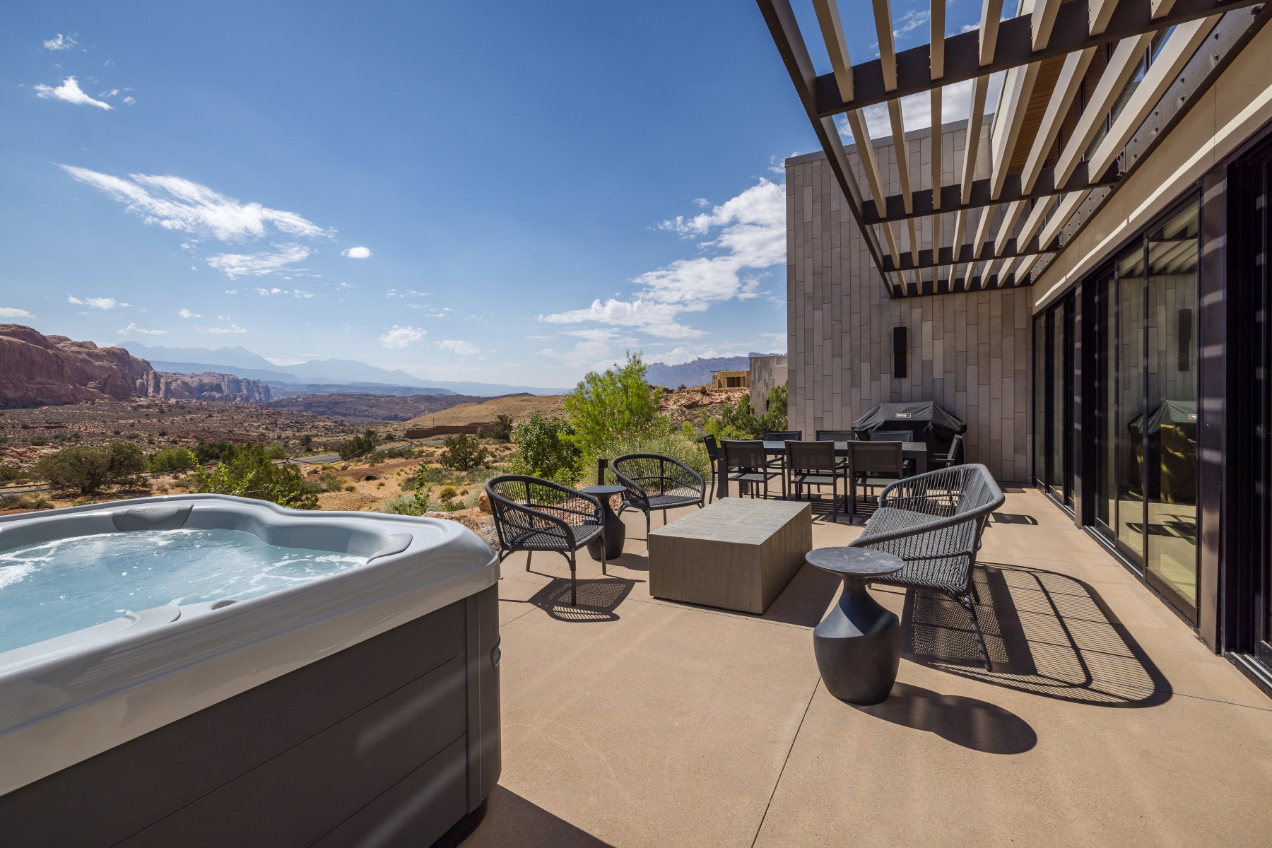 Expansive patio featuring a built-in spa, a large outdoor dining area, a built-in outdoor grill, and full-height sliding glass doors