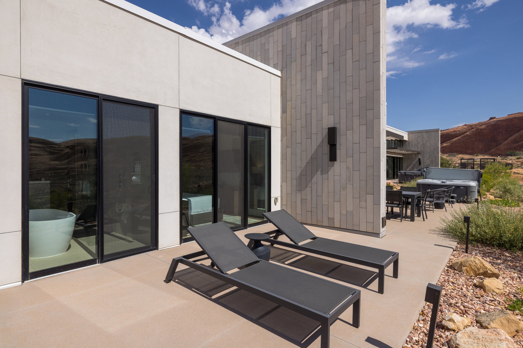 Expansive outdoor patio with concrete paving, multiple sliding glass doors, and a built-in spa