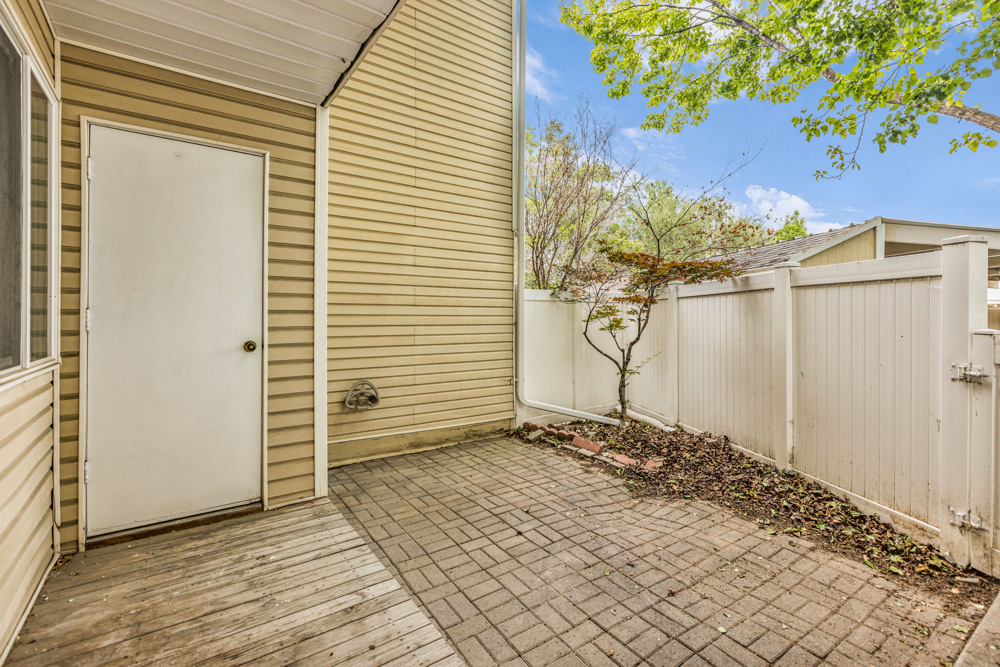 Outdoor patio area featuring textured siding, a white service door, wood-finish decking, and brick paver flooring