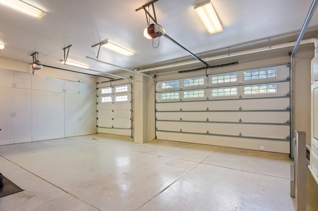 Multi-car garage featuring segmented overhead doors with transom windows, full-wall built-in cabinetry, overhead fluorescent lighting, and a sealed concrete floor