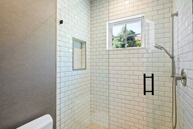 Shower enclosure featuring subway tile surround, clear glass paneling, built-in shower niche, brushed nickel showerhead and fixtures, and a high-set window