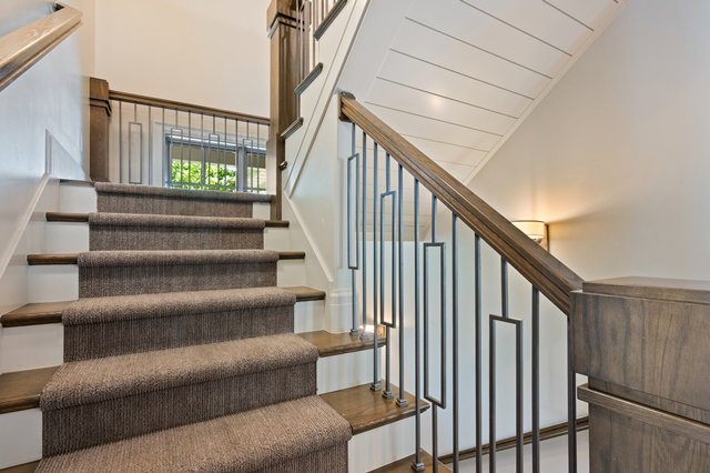 Staircase featuring wood-finish treads, a carpet runner, and a custom wrought iron railing with wood-finish handrail and newel posts