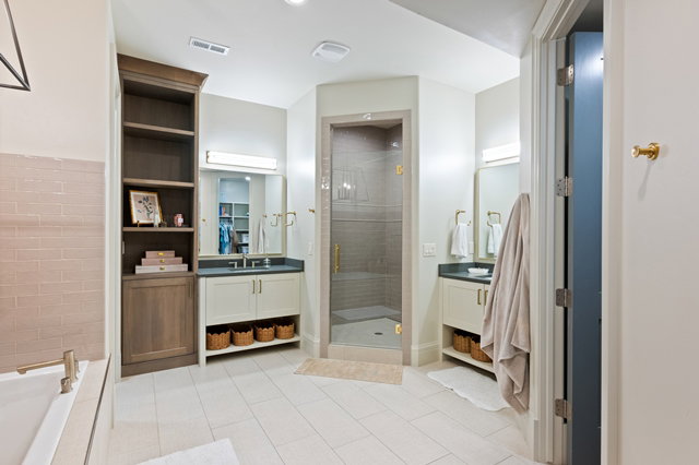Spacious bathroom featuring a glass-enclosed shower, dual vanity sinks with dark countertops, built-in shelving, and light tile flooring