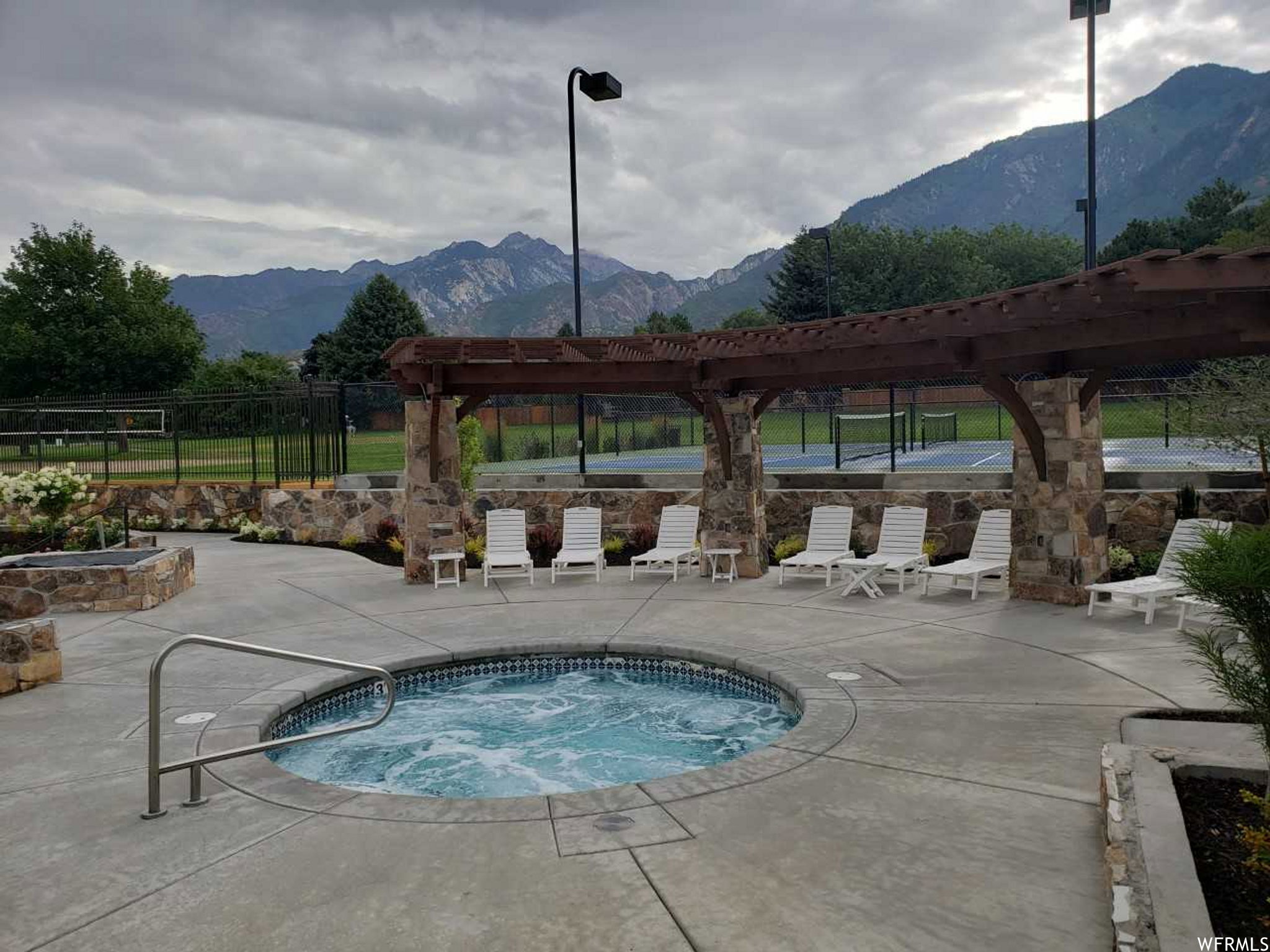 Outdoor spa featuring concrete decking, a stone-clad pergola, and integrated landscaping with mature plantings