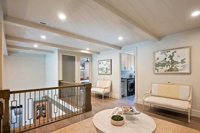 Upper level landing featuring wood-finish flooring, exposed ceiling beams, recessed lighting, and a dark wood and metal stair railing