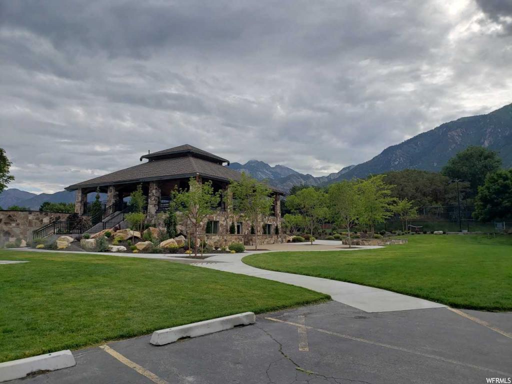 Stone-clad pavilion with a multi-tiered roofline, featuring an expansive lawn area and concrete pathways