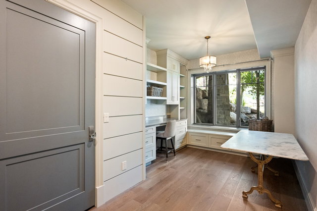 Built-in desk and cabinetry with window seating, shiplap wall accents, wood-finish flooring, and a marble-top table