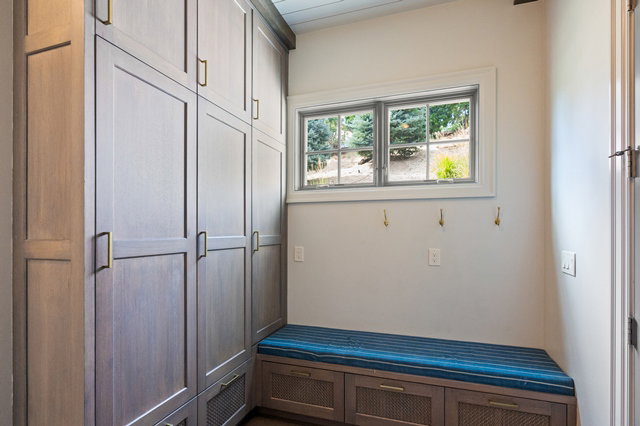 Built-in cabinetry with brass hardware, integrated bench seating with storage, and a window providing natural illumination