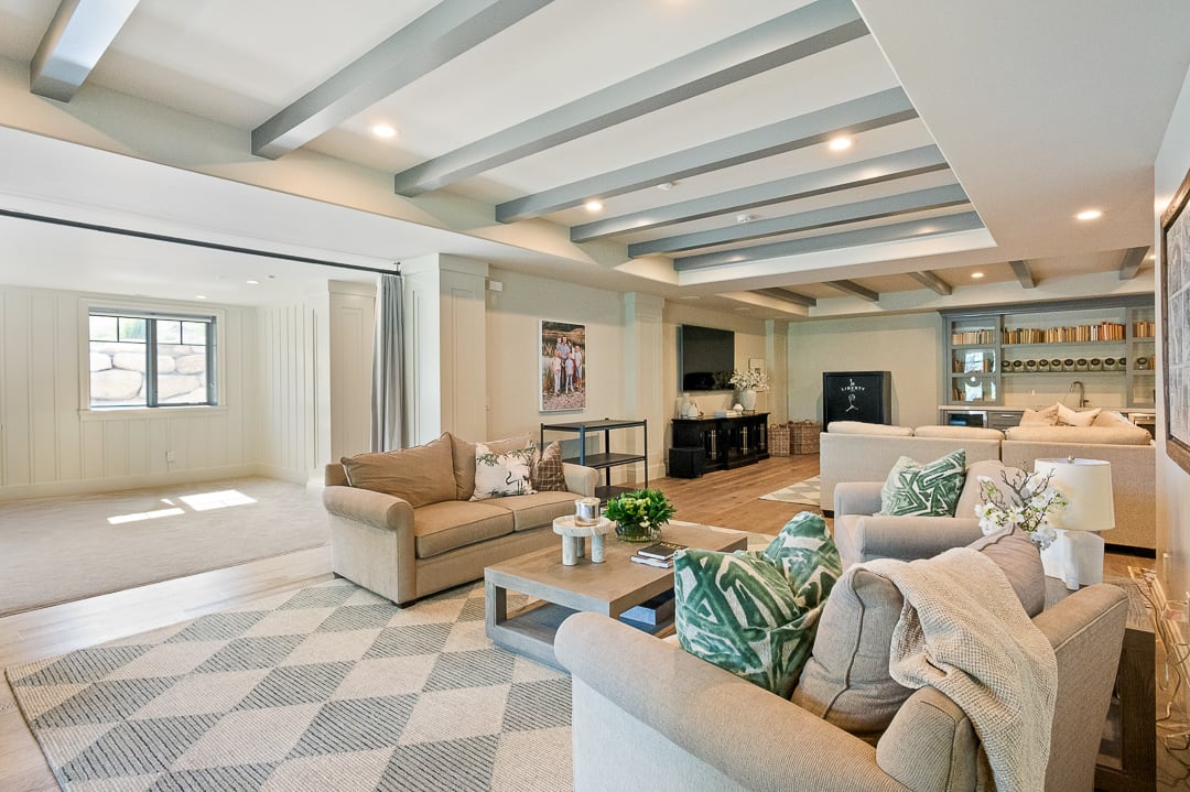 Spacious lower-level living area featuring exposed ceiling beams, recessed lighting, wood-finish flooring, and a built-in wet bar with shelving