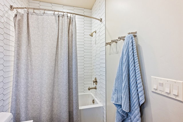 Bathroom featuring a white subway tile pattern in a vertical orientation, a white bathtub with a bronze finish shower head and faucet, and a curved shower curtain rod