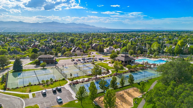 Community recreation area featuring multiple tennis courts, a large swimming pool, a shaded pavilion, and a children's play area