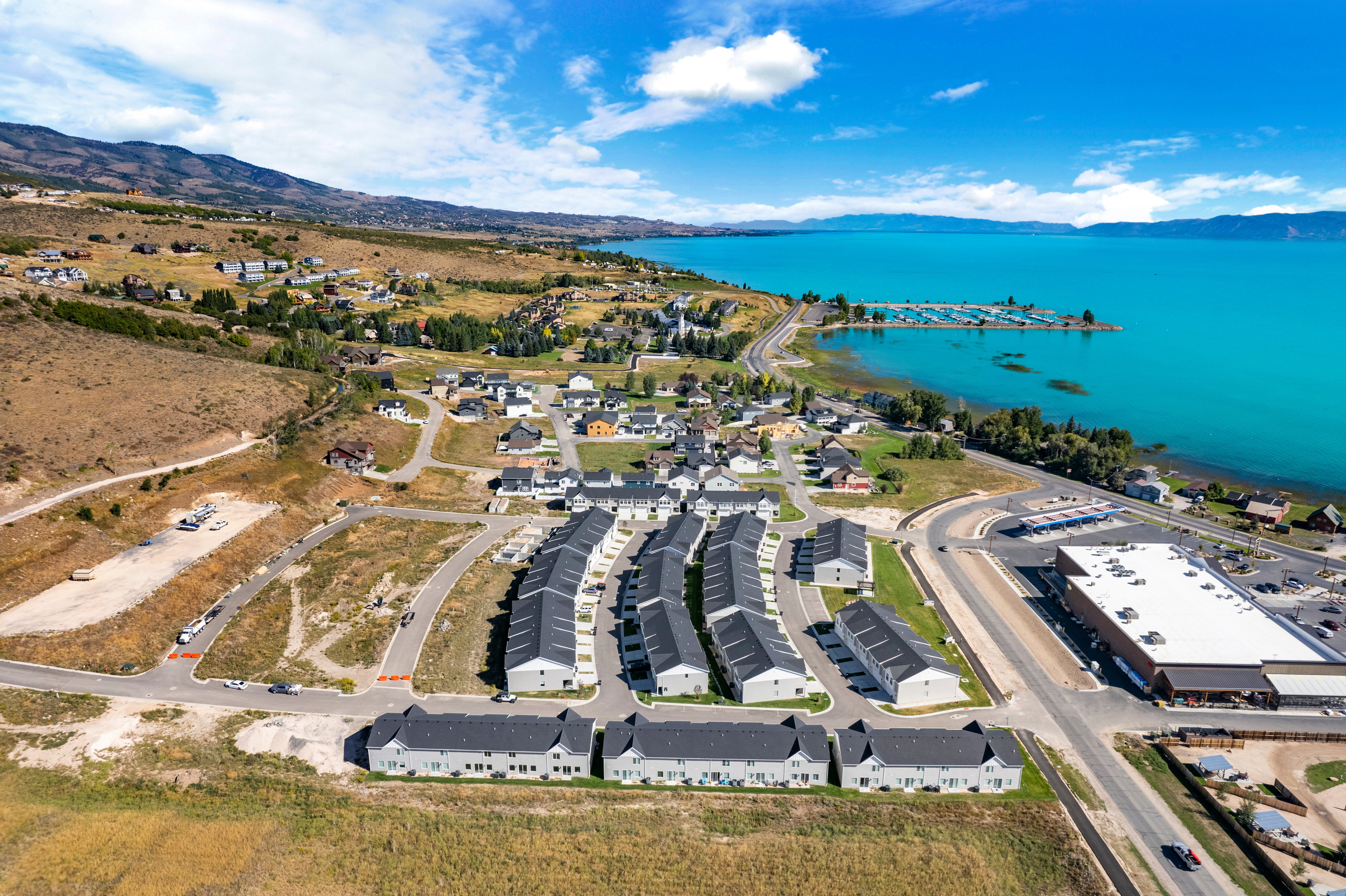 Aerial perspective showcasing a collection of residential properties with dark roofs, a marina with boats, and a large body of water