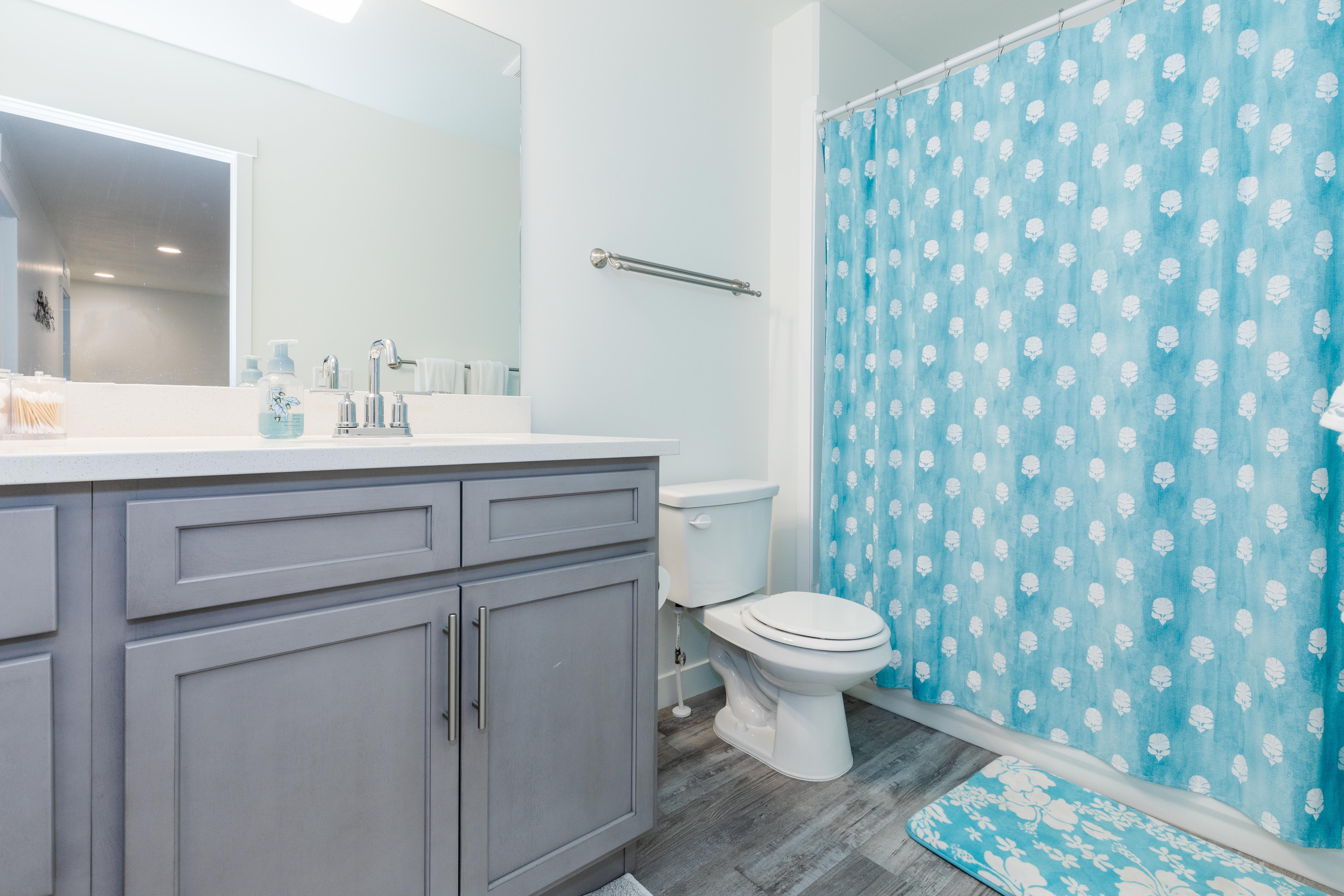 Bathroom featuring a gray shaker-style vanity with chrome hardware, a white countertop, a mirror, and wood-finish flooring
