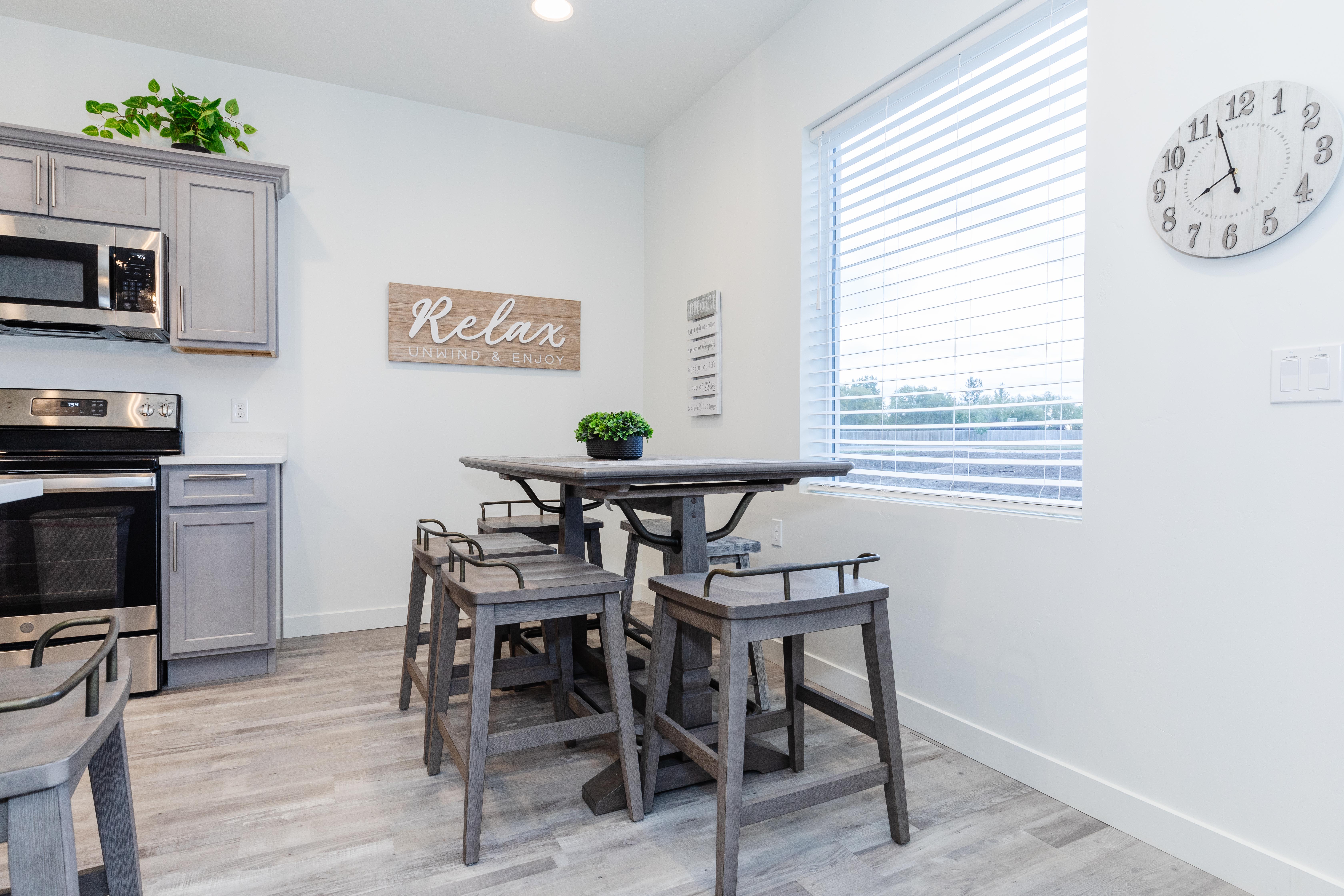 Kitchen and dining area featuring light gray cabinetry, stainless steel appliances, a white countertop, wood-finish flooring, and a large window with blinds