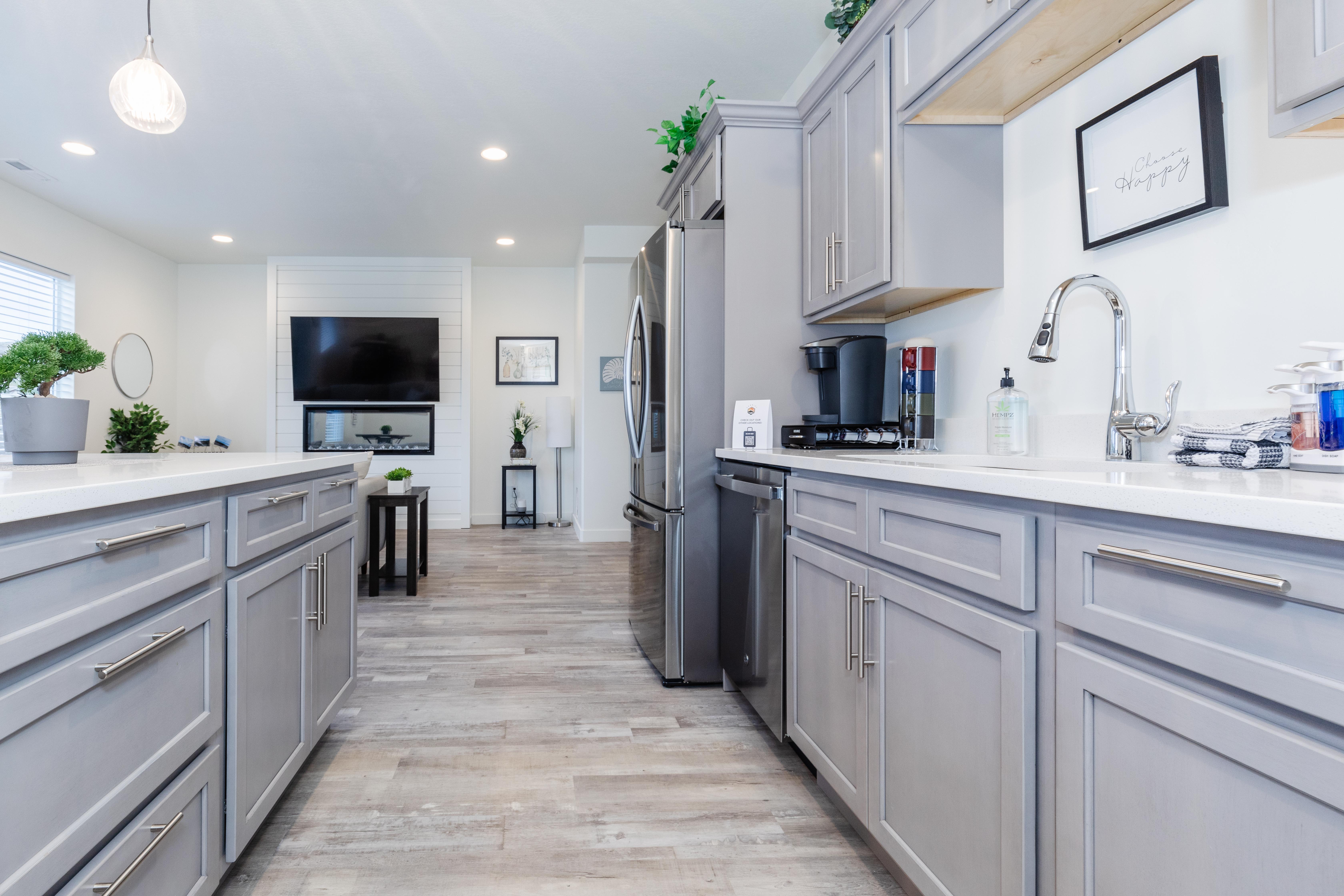 Open-concept kitchen featuring light gray cabinetry, polished chrome hardware, and white countertops