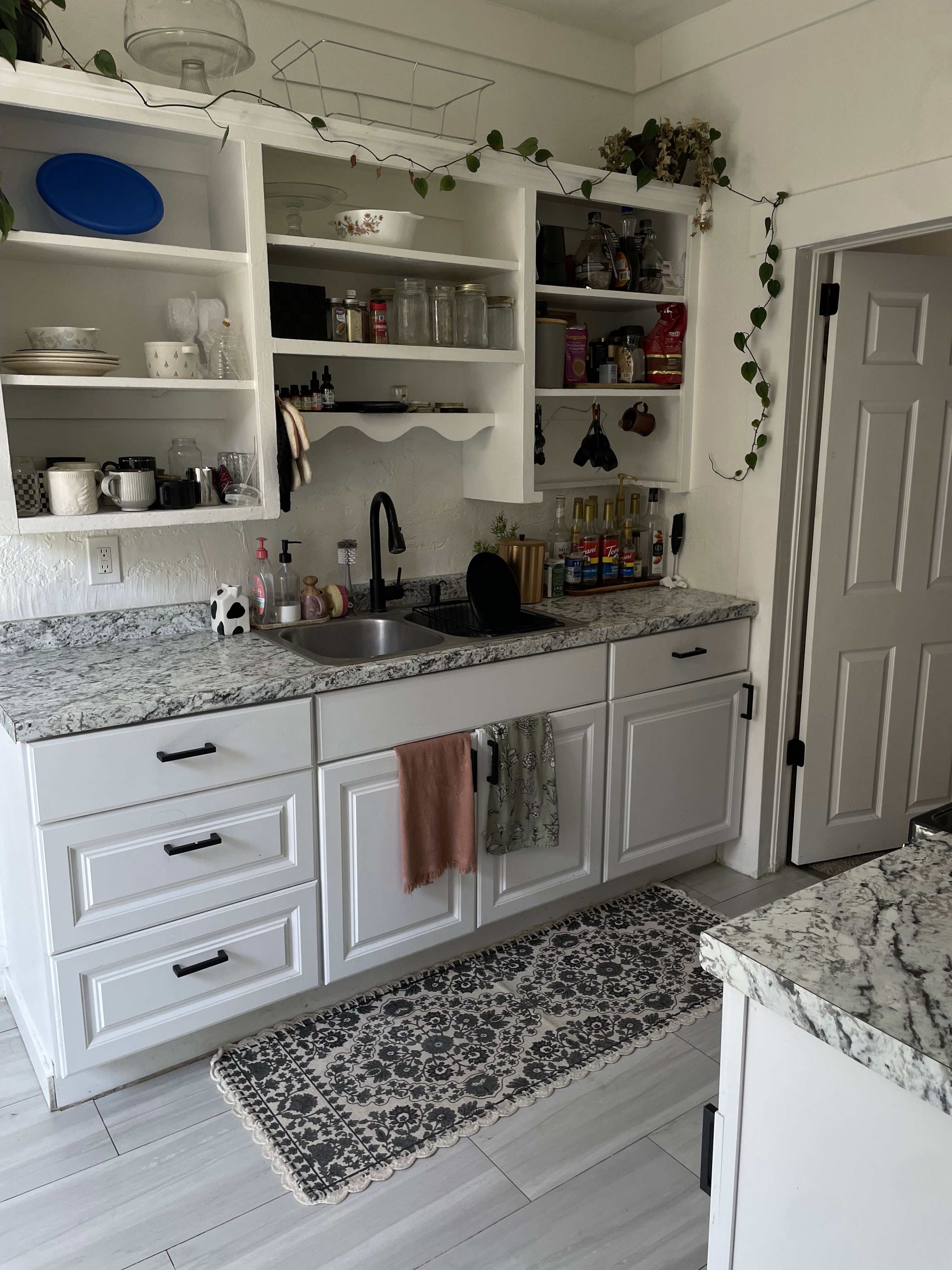 Kitchen featuring white shaker-style cabinetry, patterned stone countertops, and a dual basin sink with a matte black faucet