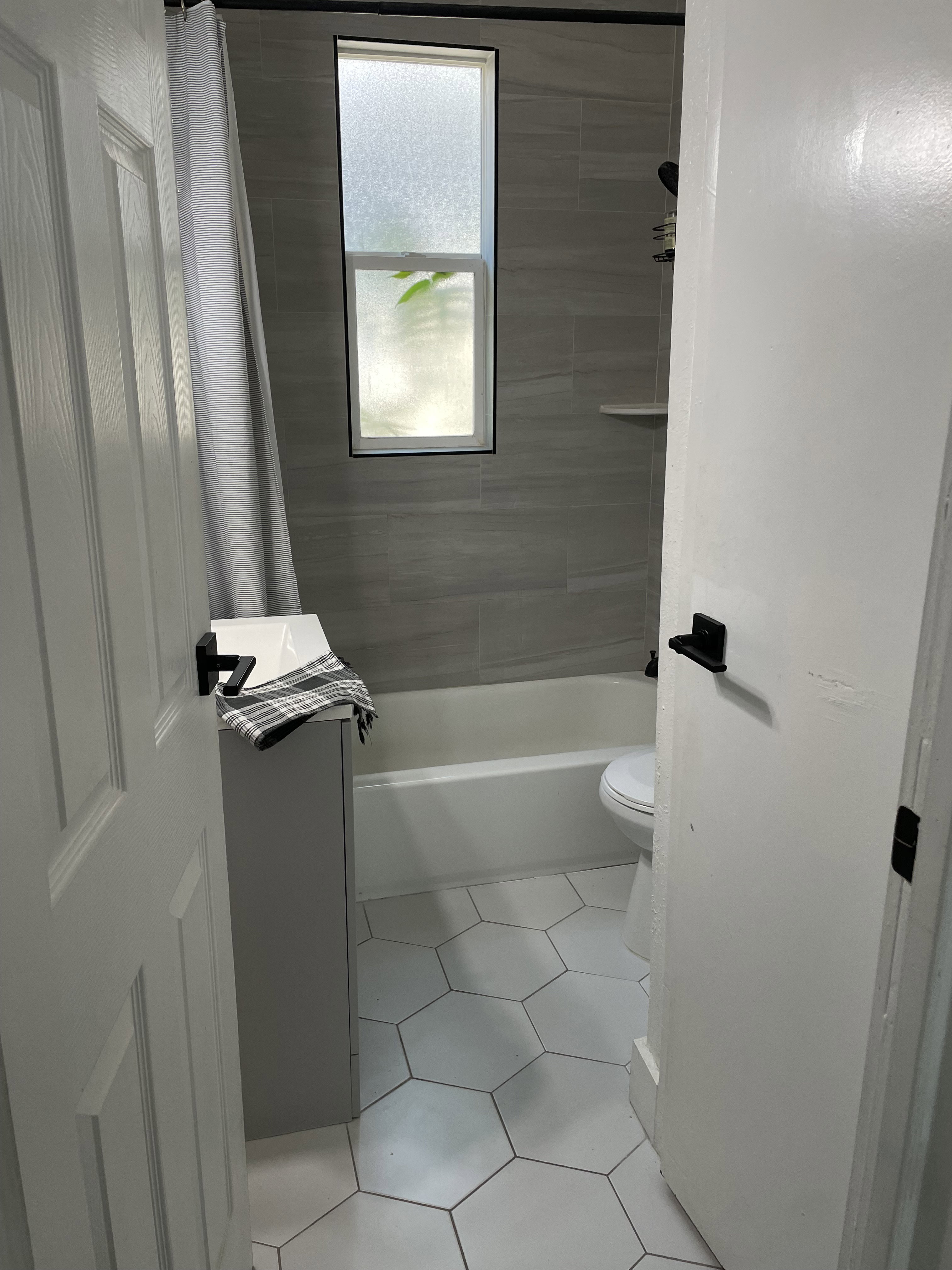 Bathroom featuring a white bathtub, gray tiled walls, white hexagonal floor tiles, and a privacy window