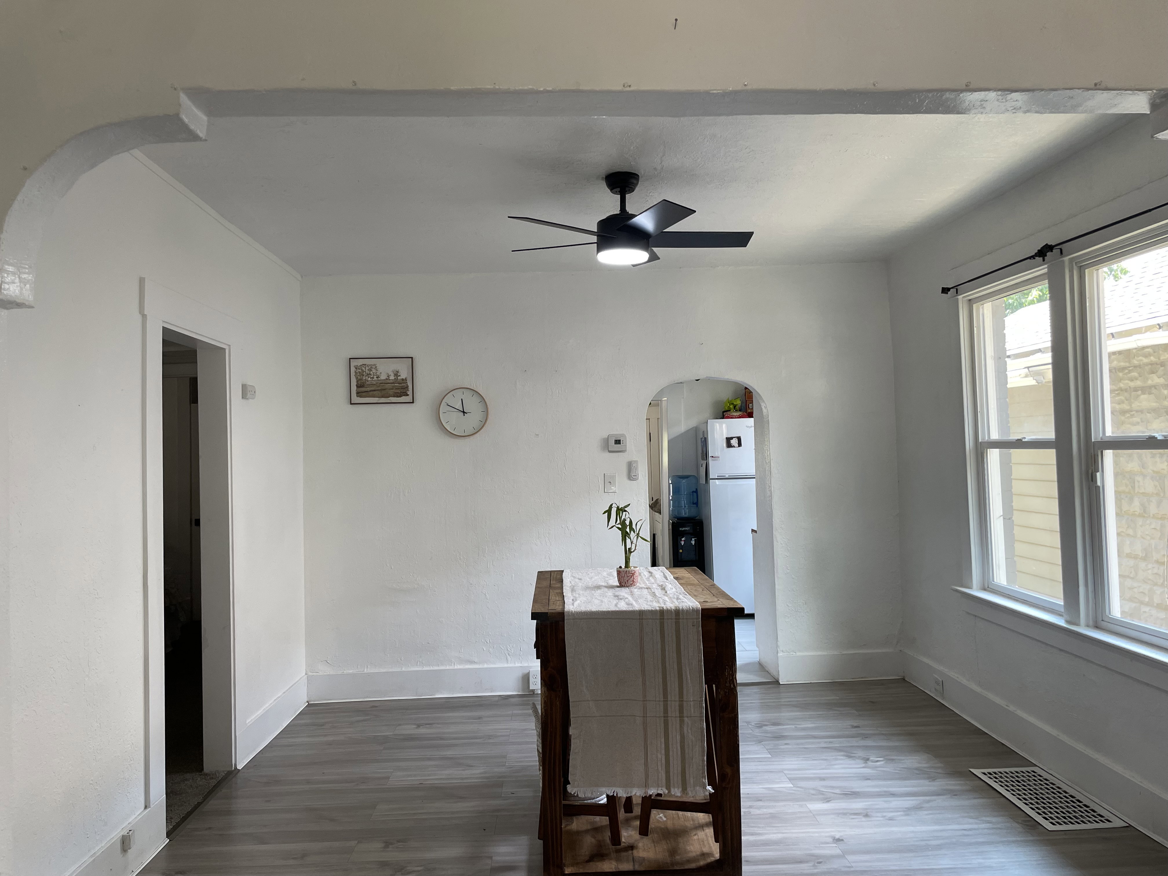 Spacious interior room featuring light-toned wood-finish flooring, white walls, and a modern ceiling fan with integrated lighting