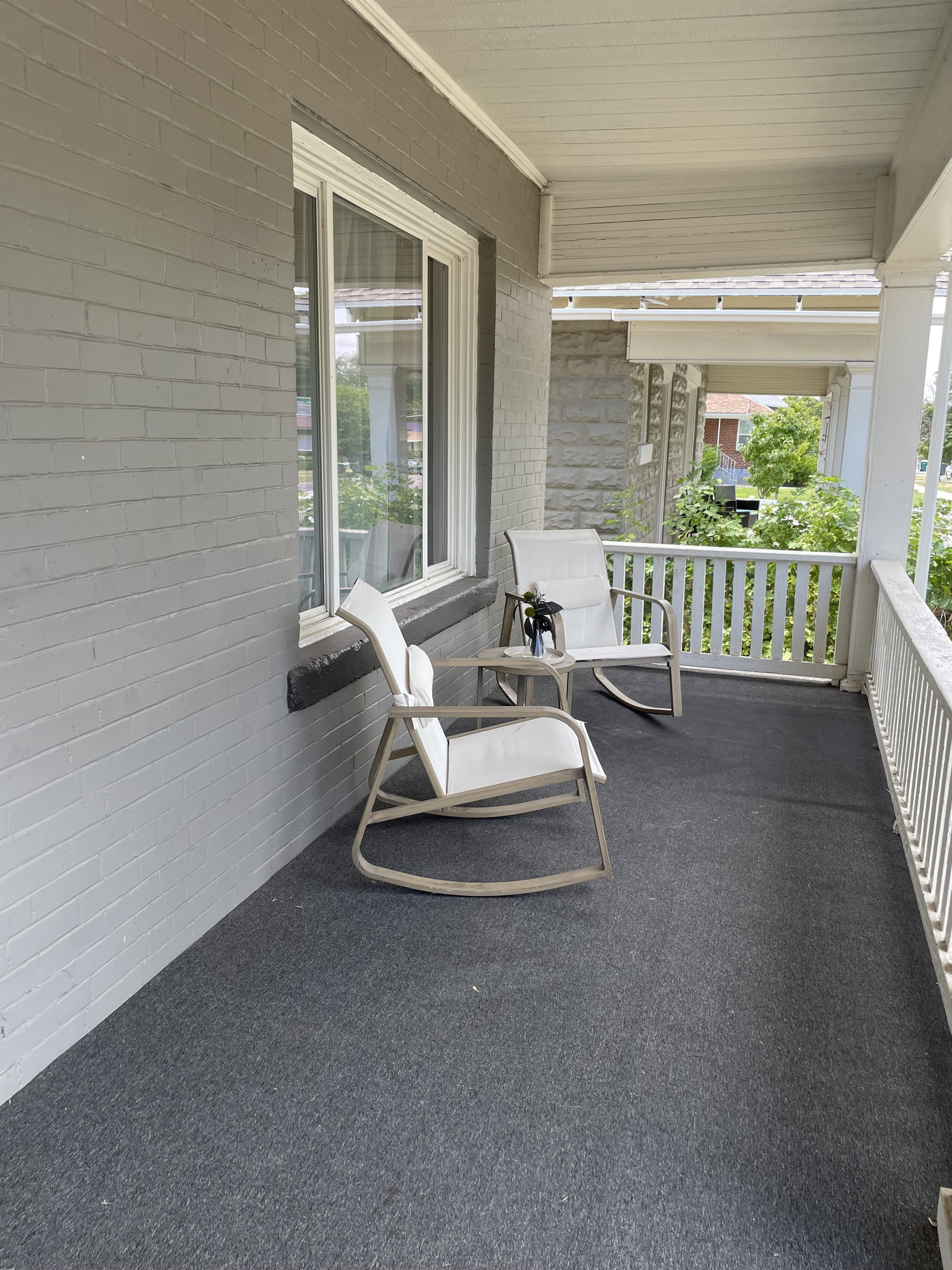Covered front porch featuring a gray brick exterior, white window trim, white porch railing, and a gray floor