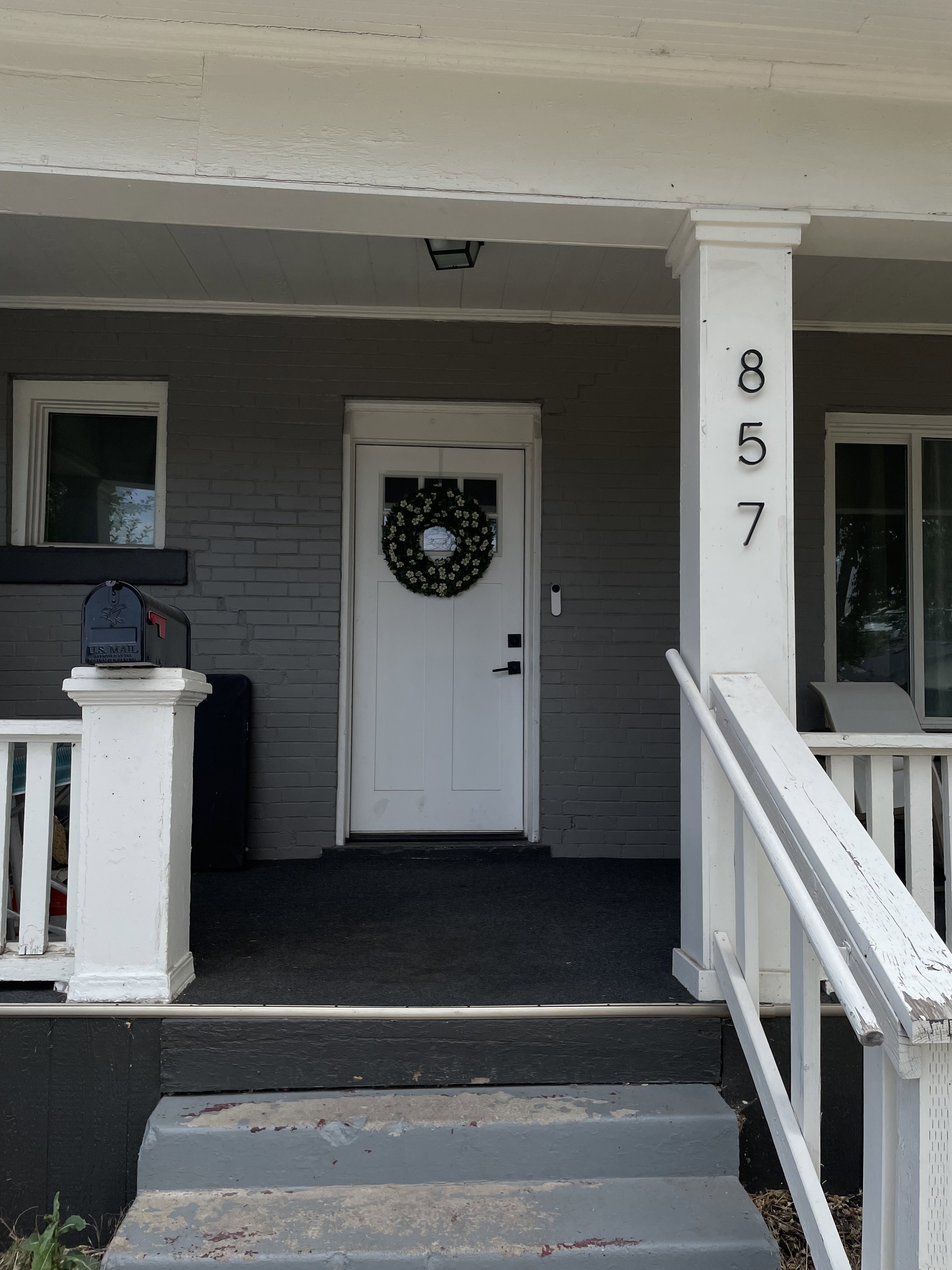 Front porch featuring a white entry door with frosted glass paneling, a dark grey painted brick facade, white trim, and white porch columns