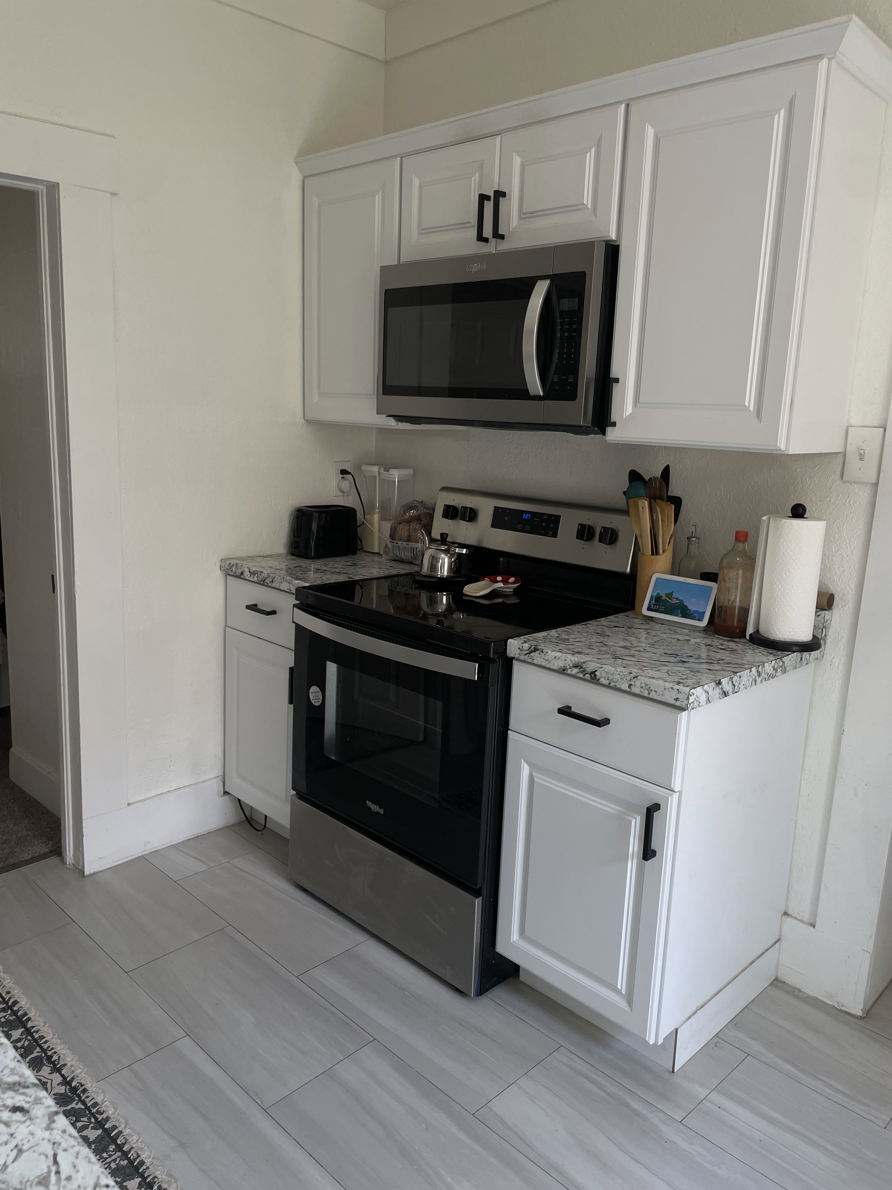 Kitchen area featuring white cabinetry with dark hardware, a stainless steel microwave, a stainless steel range, granite-style countertops, and light-toned tile flooring