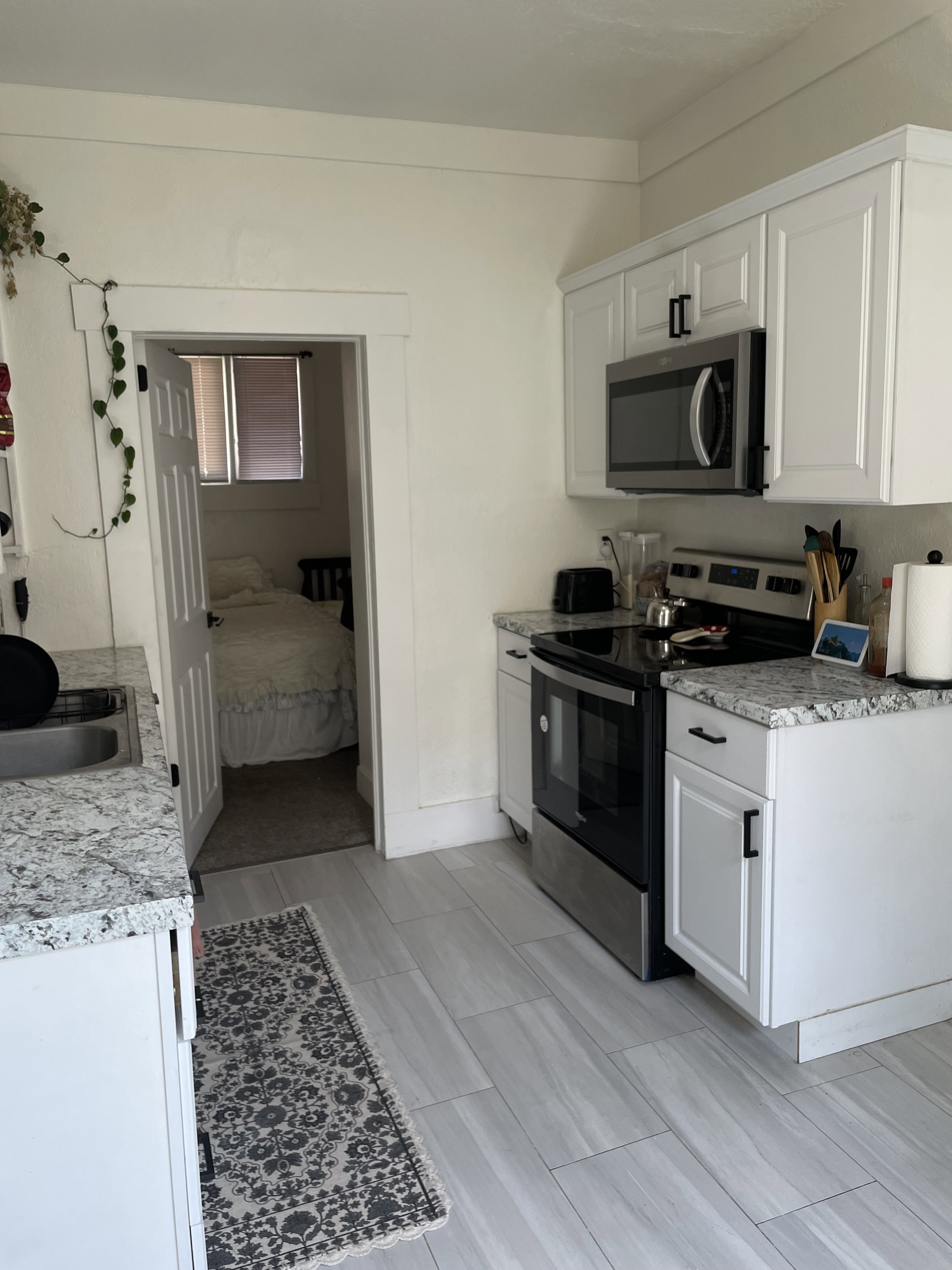 Kitchen featuring white shaker cabinetry, stainless steel appliances, granite countertops, and wood-finish tile flooring