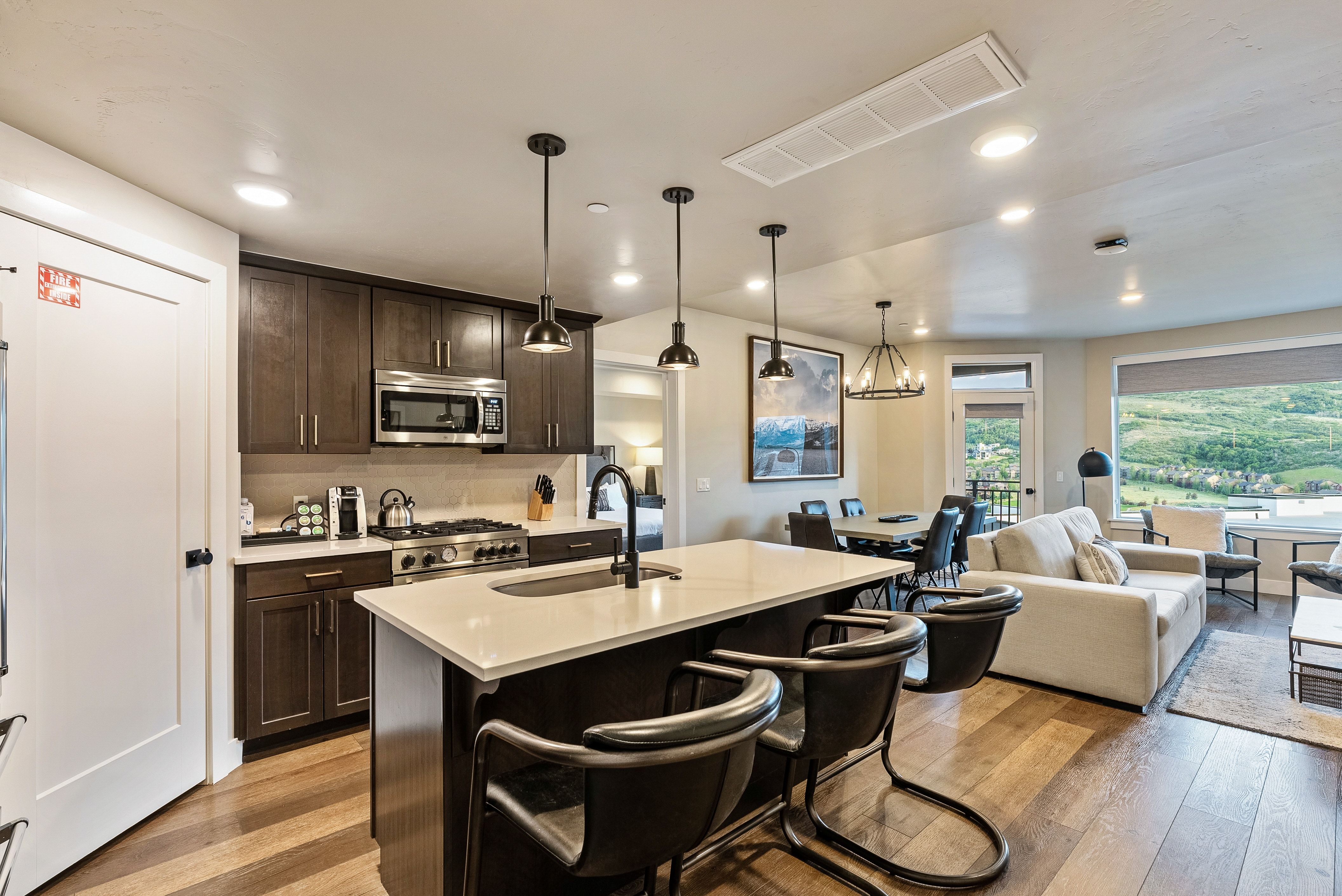 Open-concept kitchen and living area featuring a large center island with seating, dark wood cabinetry, stainless steel appliances, and wood-finish flooring