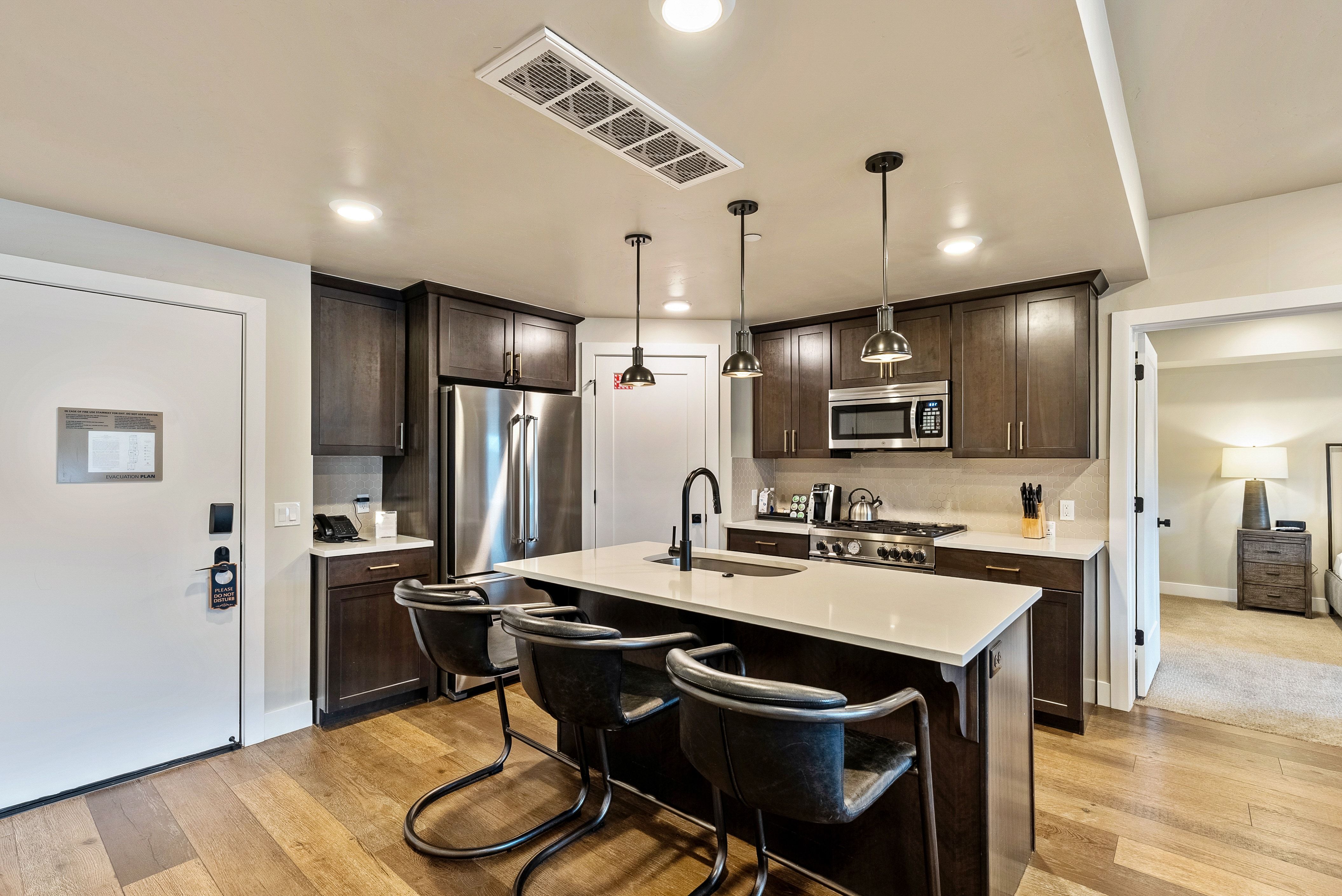 Modern kitchen featuring wood-finish flooring, dark wood cabinetry, stainless steel appliances, a center island with seating, and pendant lighting