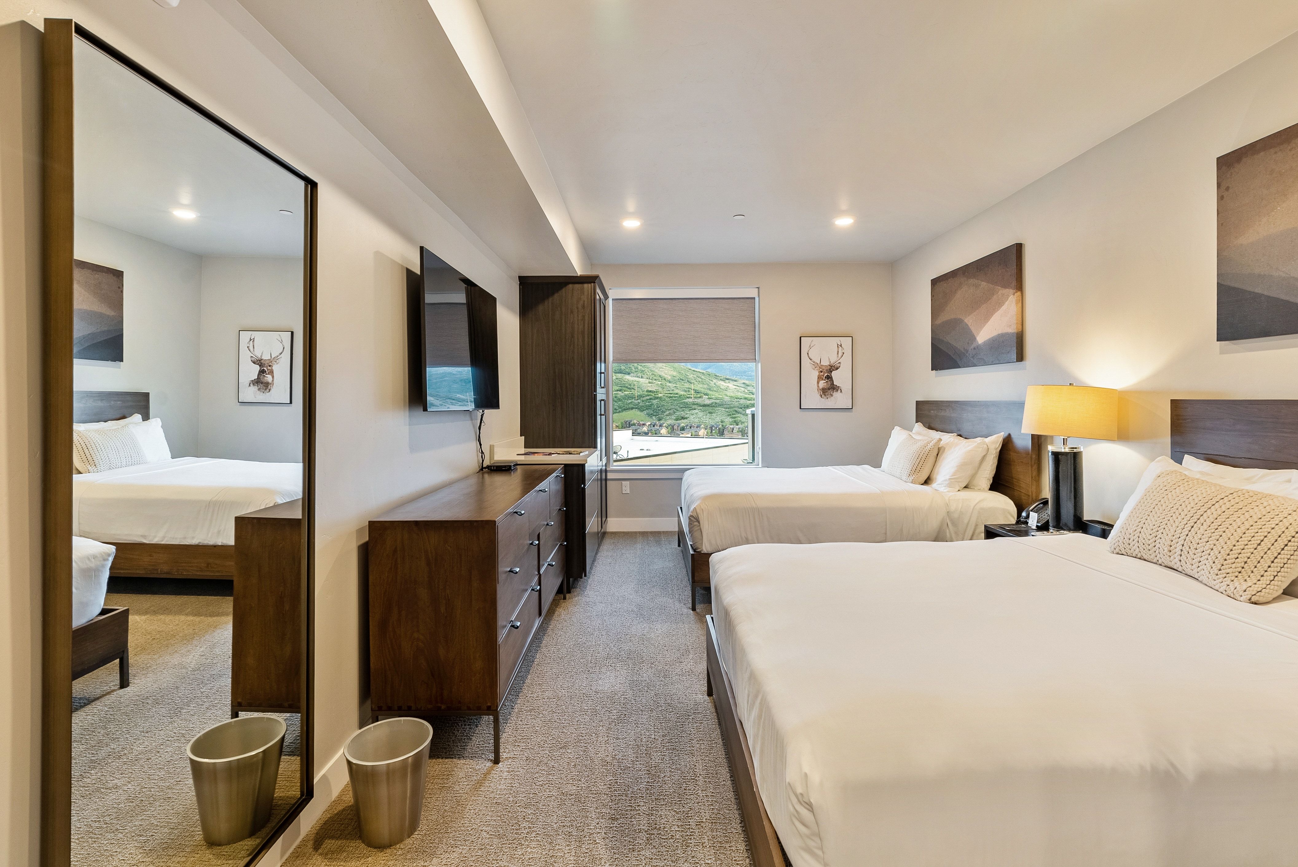 Bedroom featuring two beds, carpeted flooring, and a large window with a roller shade