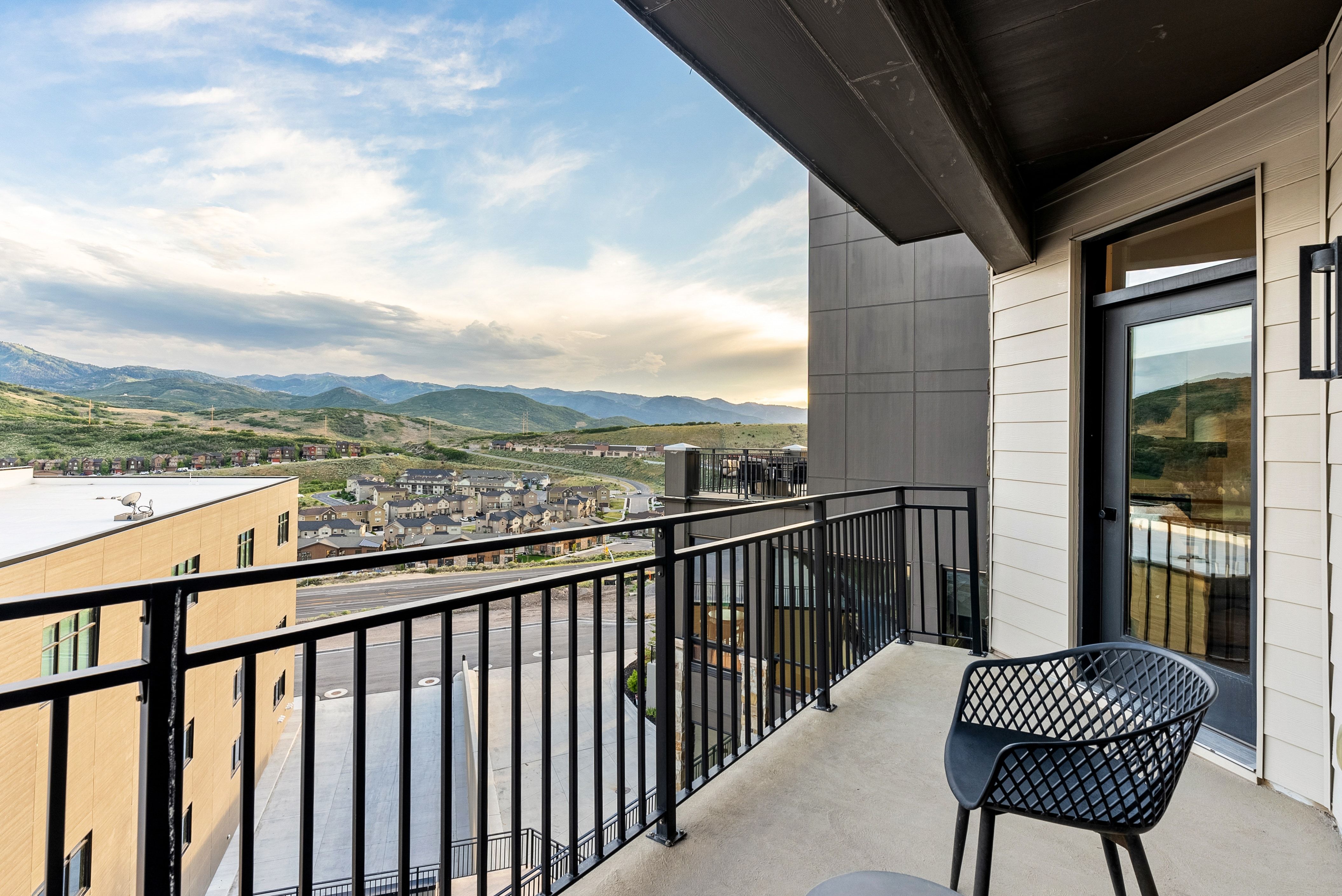 Private concrete balcony with black metal railing, featuring a full-light exterior door with black trim, and a contemporary black wall sconce