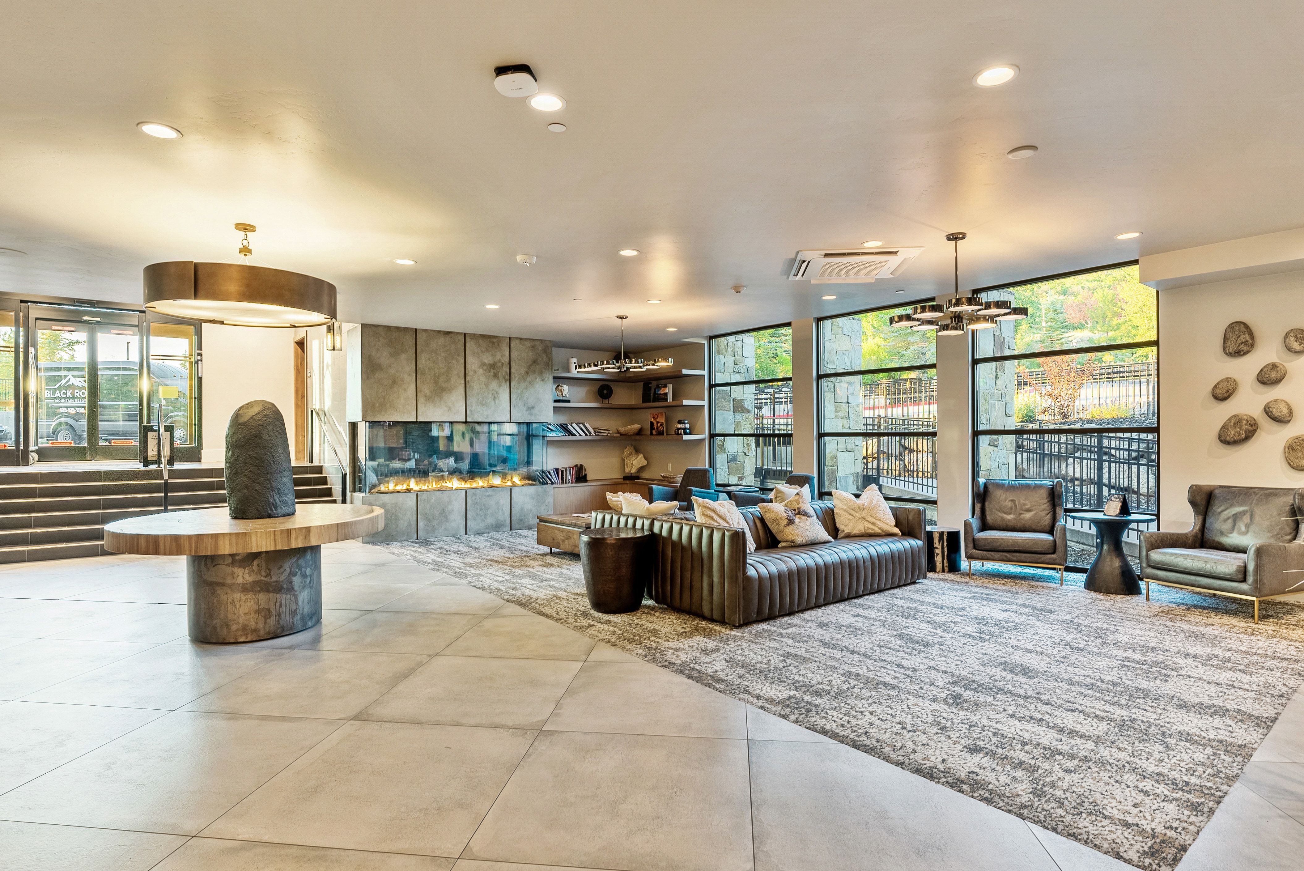 Spacious common area featuring large format tile flooring, a linear fireplace with stone-look surround, and extensive window walls