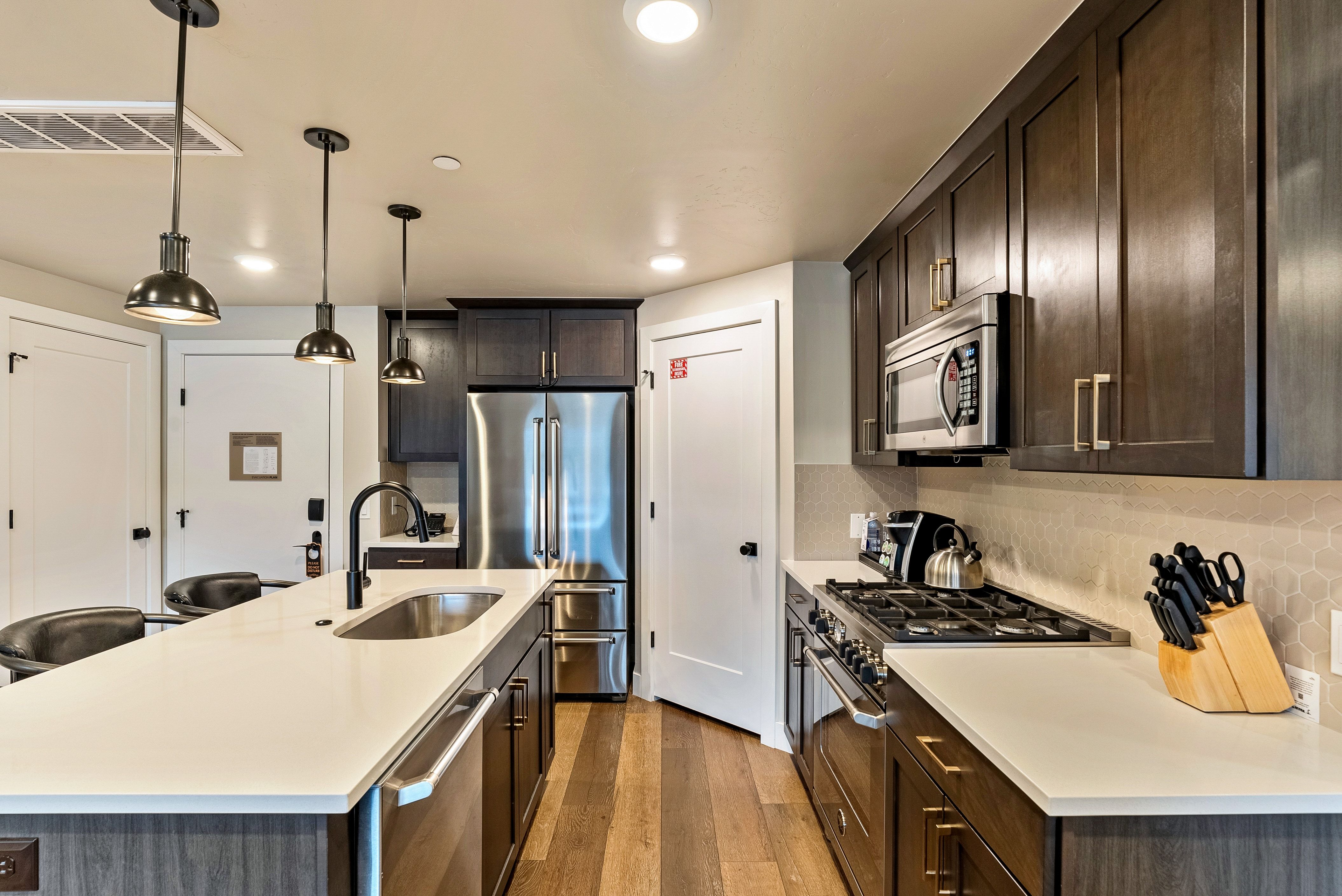 Modern kitchen featuring a large island with sink, stainless steel appliances, dark wood cabinetry, light countertops, and wood-finish flooring