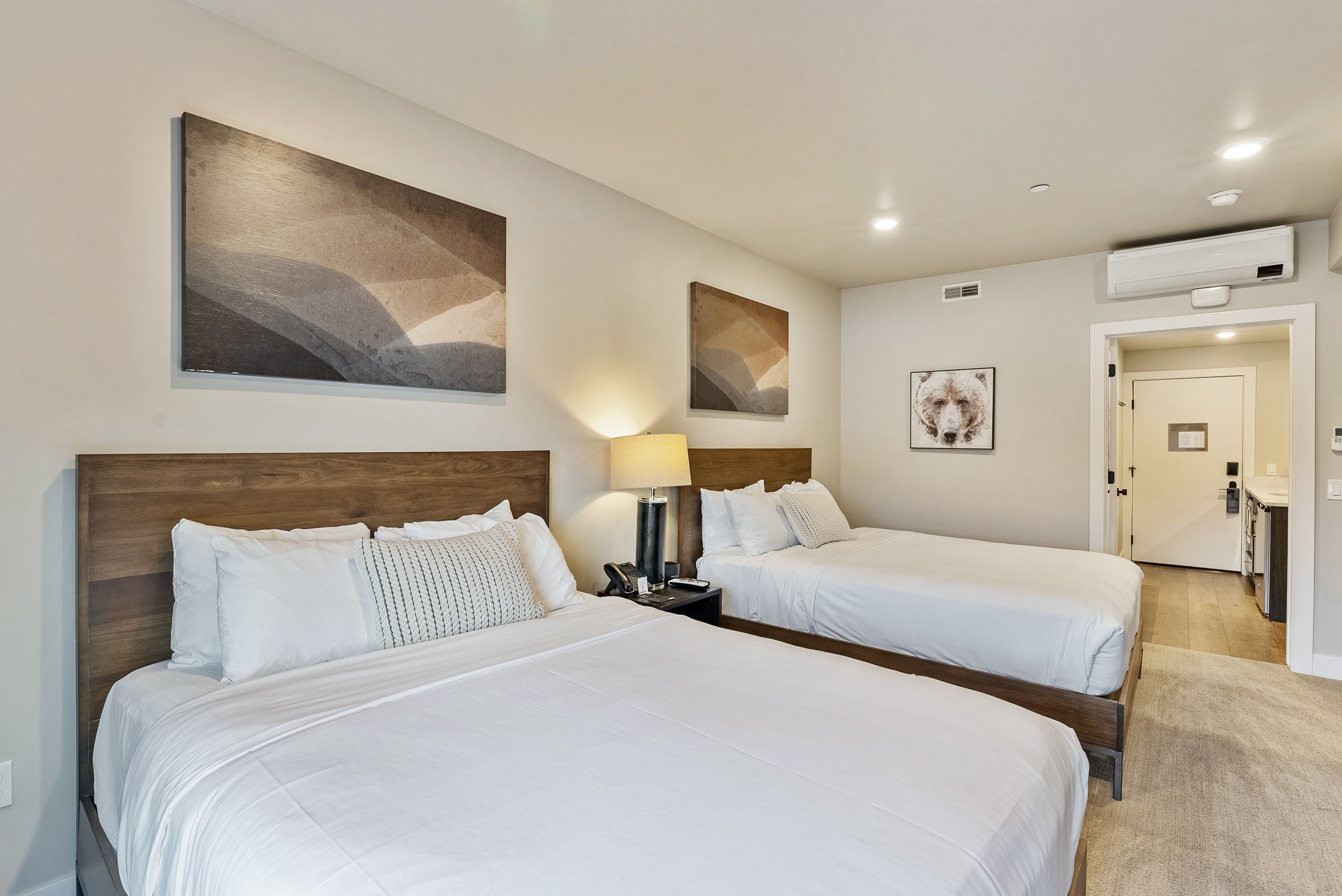 Bedroom featuring two wood-frame beds with matching wood headboards, recessed ceiling lighting, a wall-mounted climate control unit, and wood-finish flooring