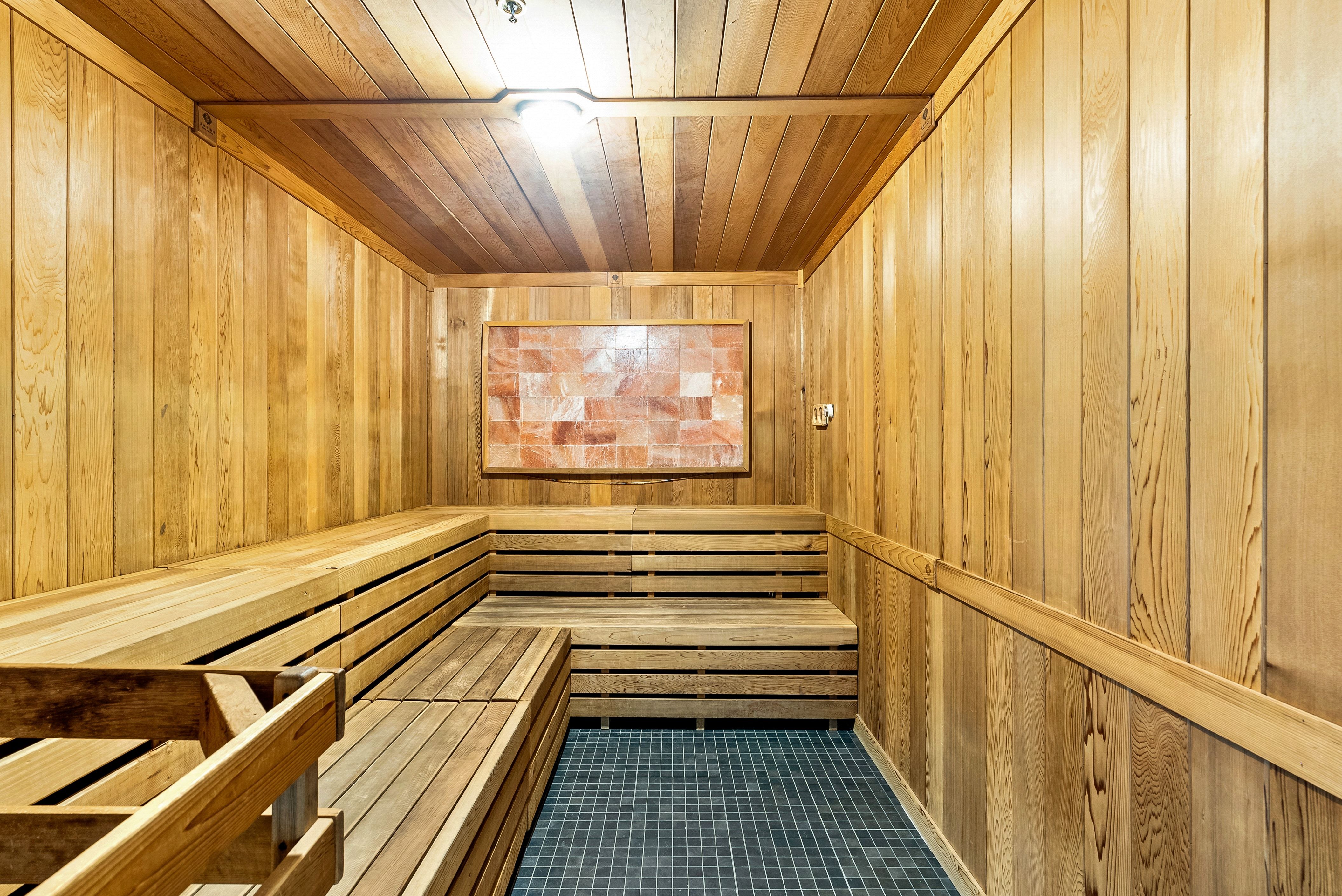Sauna with comprehensive wood paneling, multi-level slatted wood benches, a dark mosaic tile floor, and a Himalayan salt block feature wall
