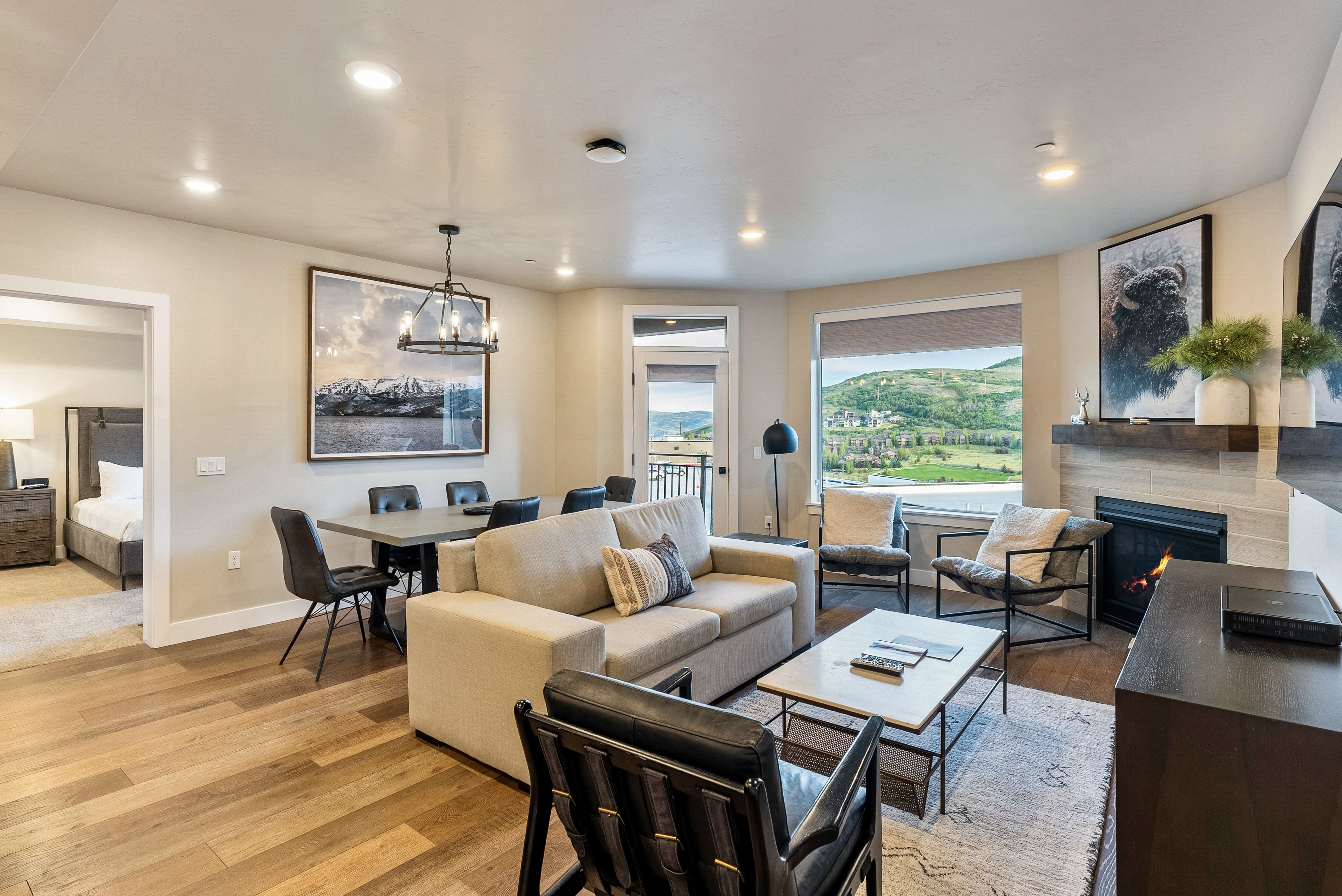 Open-concept living area featuring wood-finish flooring, a modern fireplace with a wooden mantel, recessed lighting, and a dining area with a chandelier