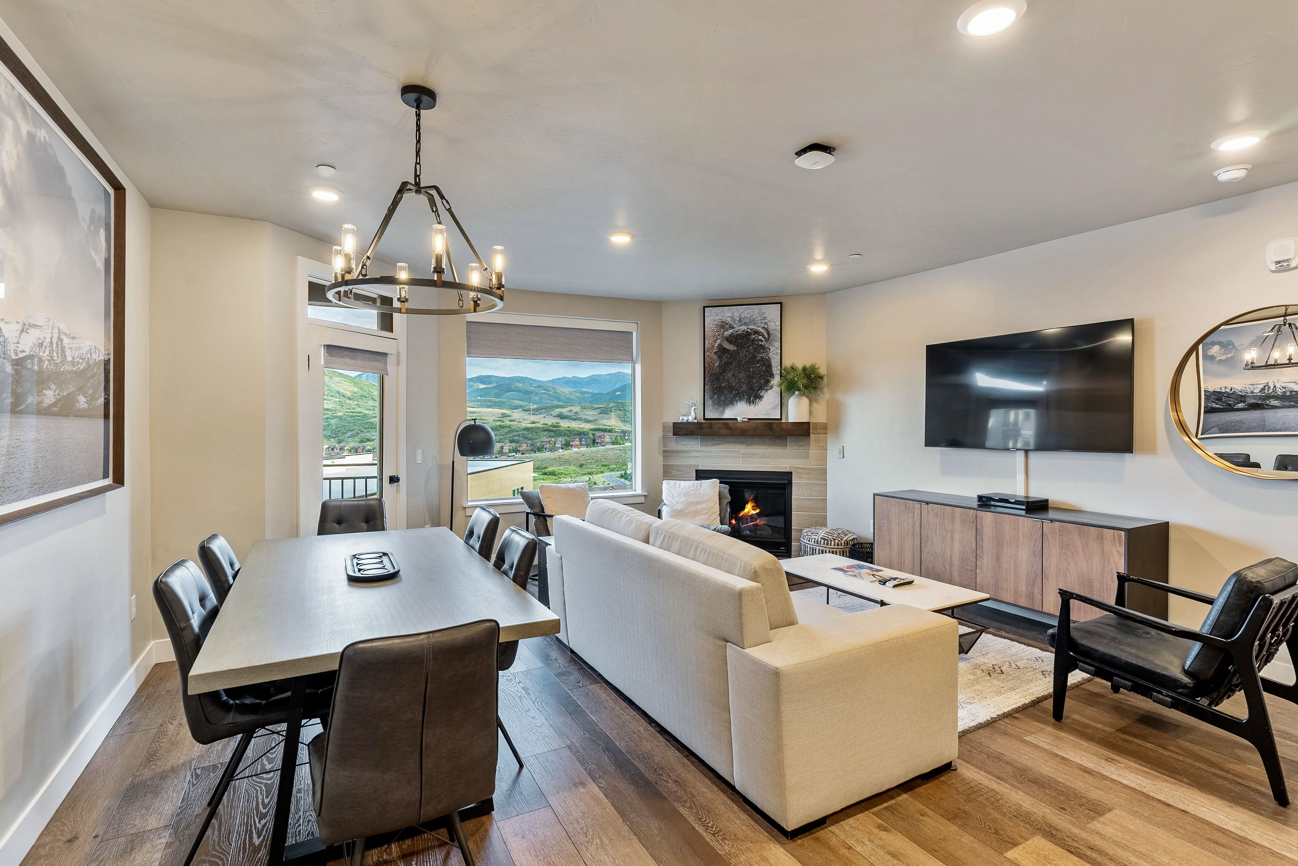 Open concept living space featuring wood-finish flooring, a contemporary chandelier, recessed lighting, a built-in fireplace with stone surround, and large windows with mountain scenery